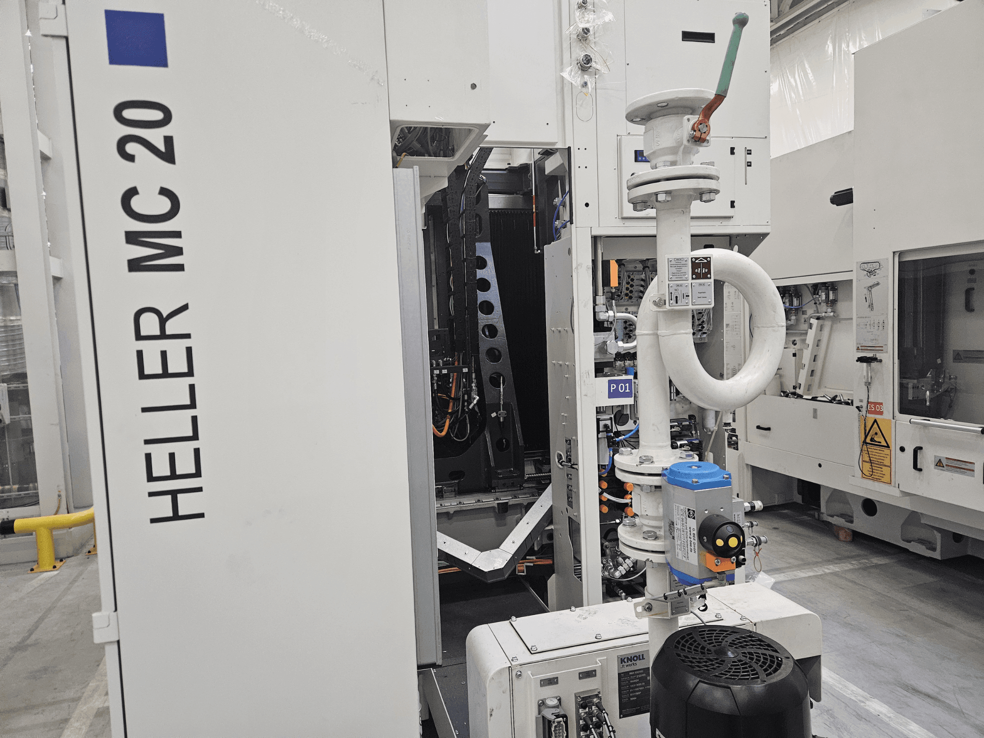 "Heller MC 20" mašina gamykloje, kurioje matomas valdymo skydelis ir mechaniniai komponentai iš šono.