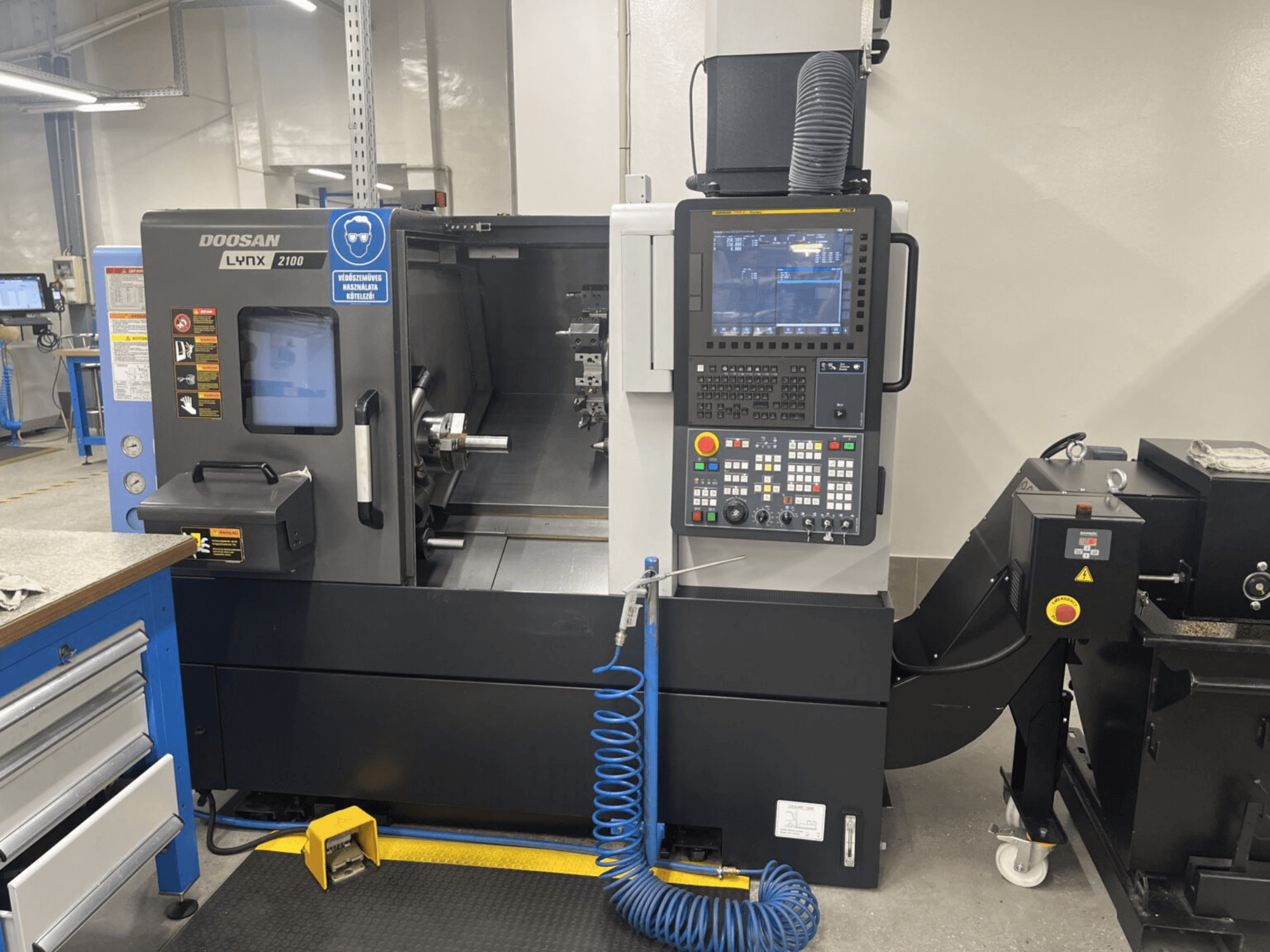 Horizontaliųjų tekinimo staklių "DOOSAN Lynx 2100A" priekinis vaizdas, kuriame matomas valdymo skydelis ir verpstės zona su svarbiomis saugos funkcijomis.