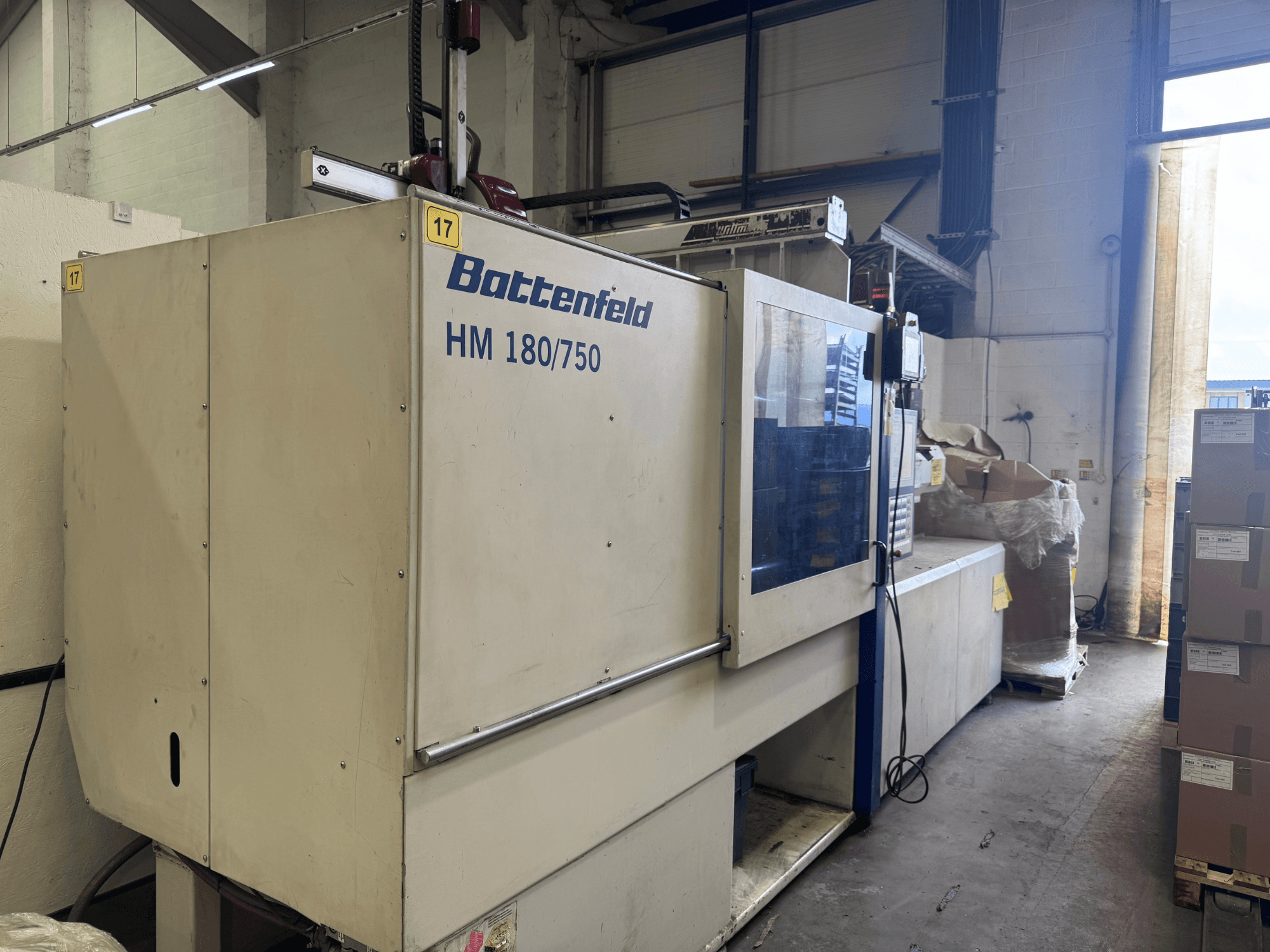 "Battenfeld HM150750" hidraulinė įpurškimo mašina, žiūrint iš priekio, su valdymo pultu ir aplinkiniais įrenginiais.