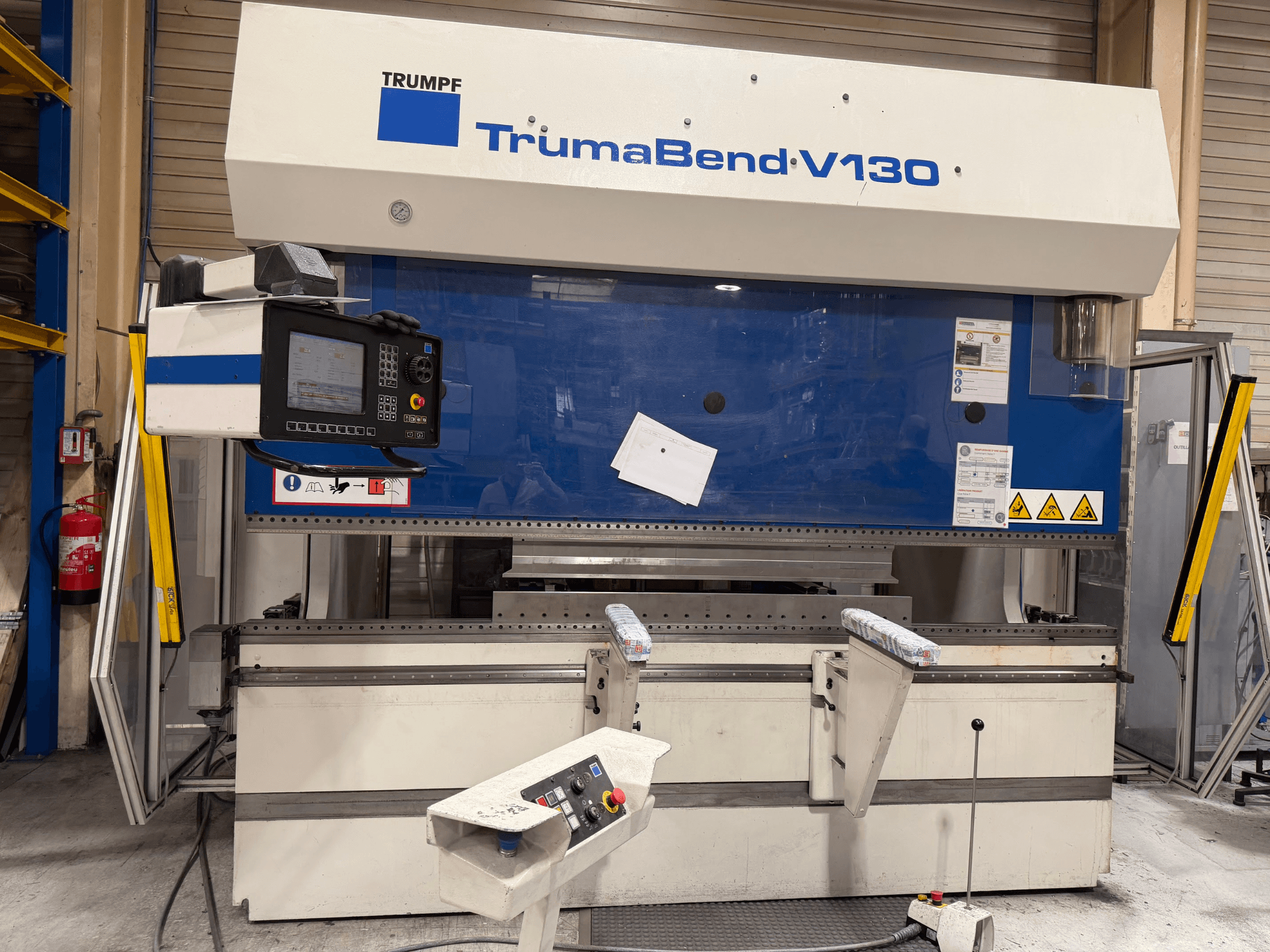 „TRUMPF TrumaBend V130“ lenkimo presas gamyklinėse sąlygose, su valdymo pultu ir saugos įranga, vaizdas iš priekio.