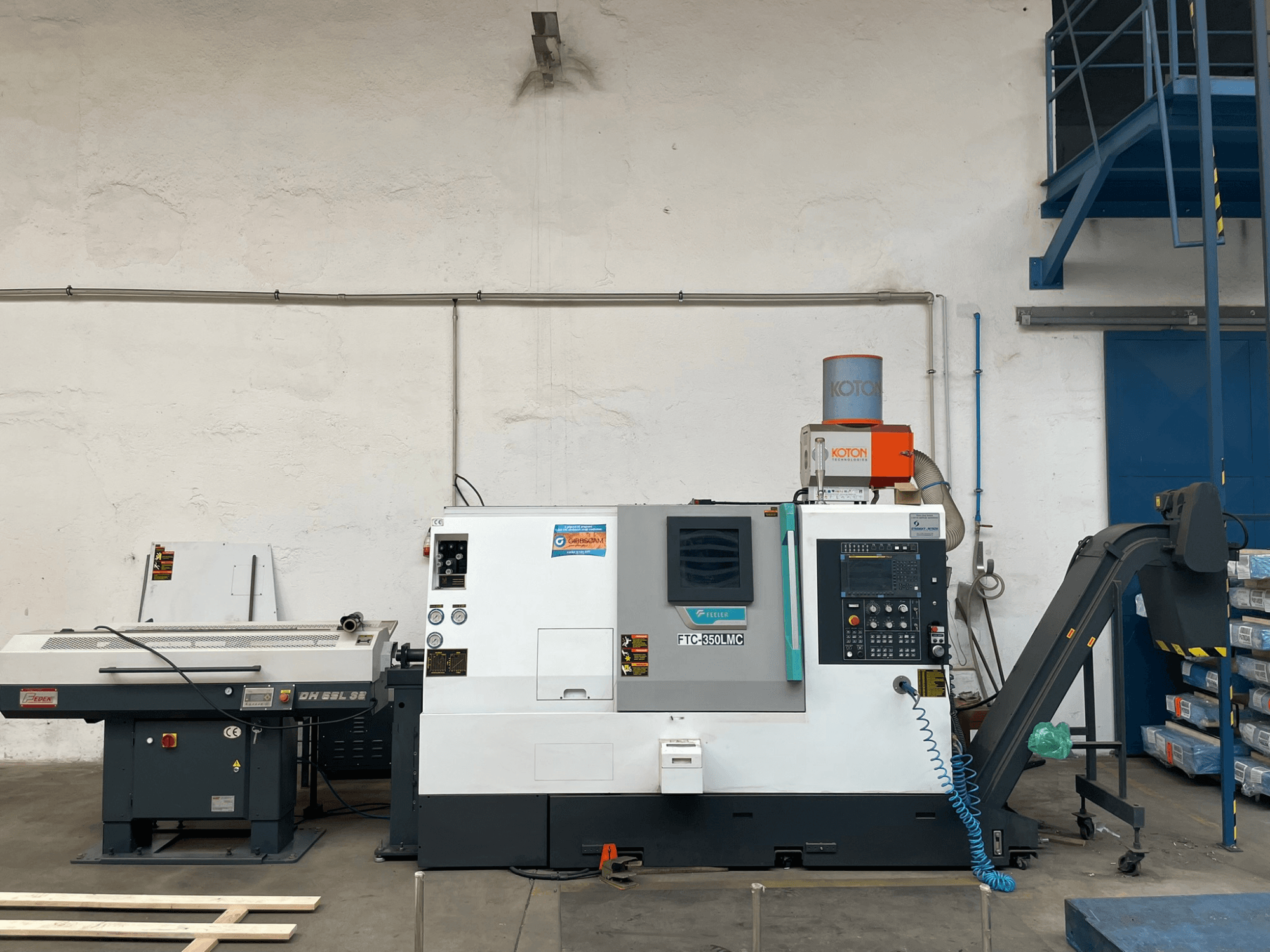 Feeler FTC 350 LMC horizontalios tekinimo staklės dirbtuvėse, kuriose matomas valdymo skydelis ir įrankių tiekimo linijos. Vaizdas iš šono.