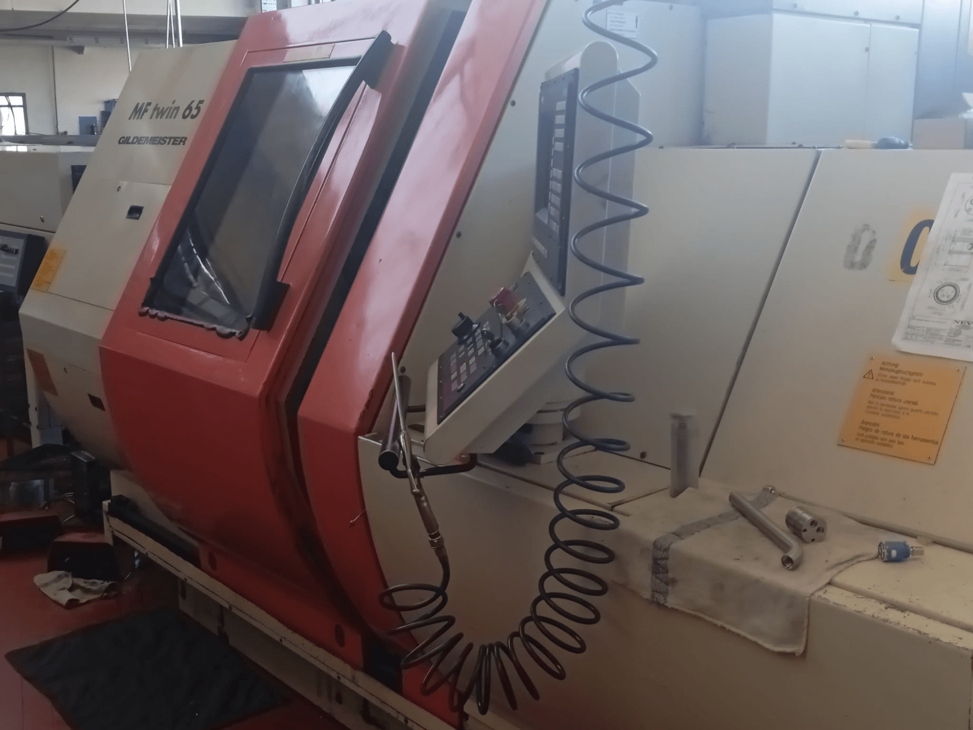 Oranžinės ir baltos spalvos MF Twin 65 Gliedemeister mašina, vaizdas iš priekio, valdymo skydelis ir įrankiai ant audinio.