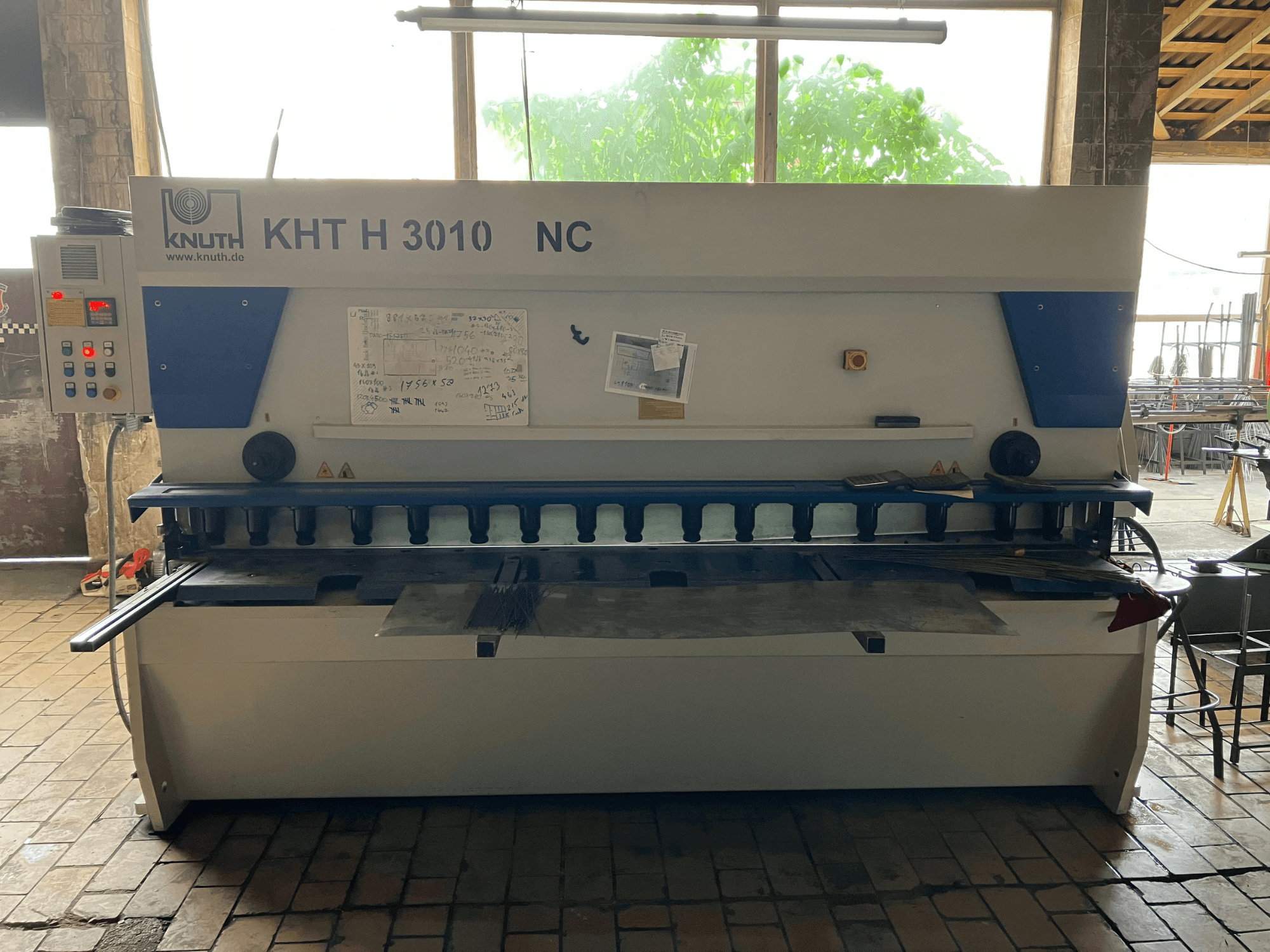 Hidraulinė kirpimo staklė „KNUTH KHT H 3010 NC“, vaizdas iš priekio, su valdymo pultu ir metalo pjovimo zona.