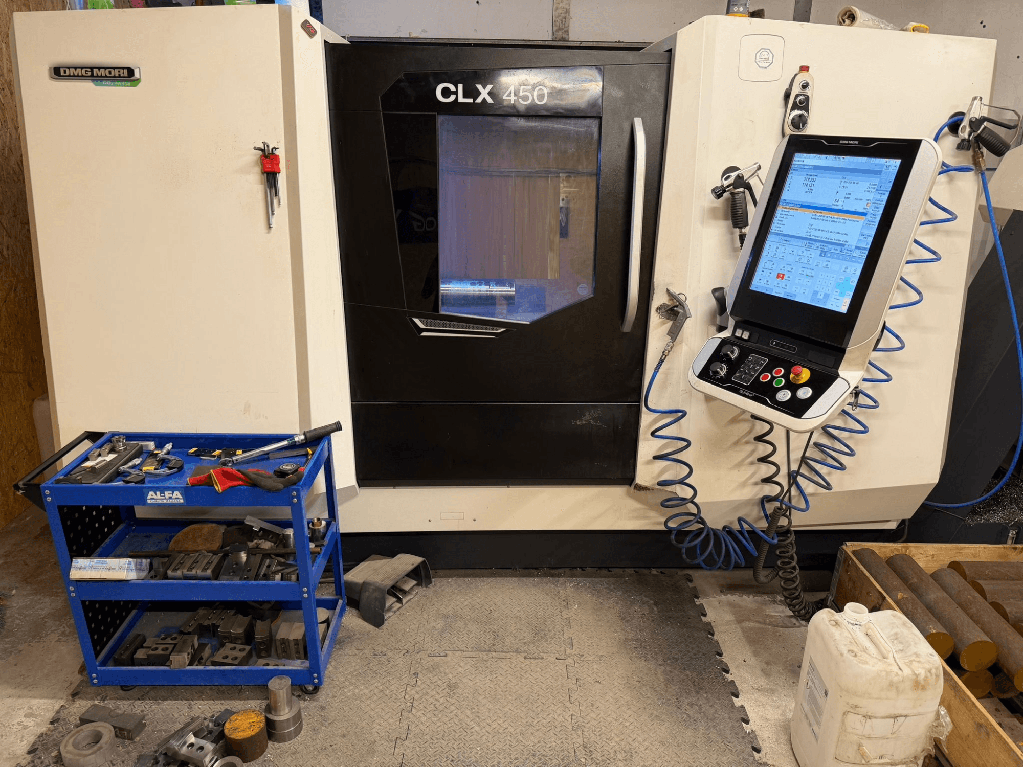 DMG MORI CLX 450 V3 horizontaliojo tekinimo staklių priekinis vaizdas, kuriame matyti valdymo skydelis ir šalia esantis įrankių vežimėlis su įranga.