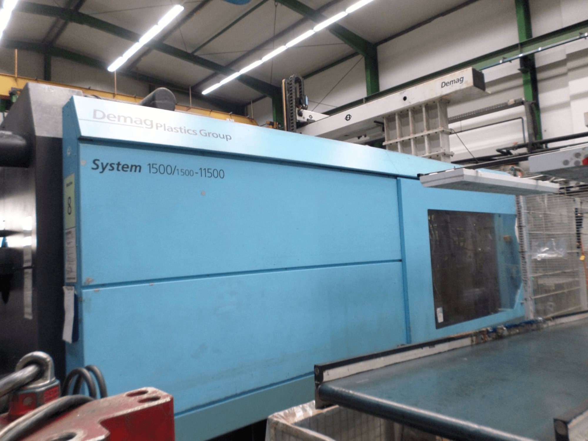 Mėlynos spalvos hidraulinė liejimo mašina „Demag D 650“, šoninis vaizdas, kuriame matoma „System 1500/1500-11500“ etiketė ir darbo zona.