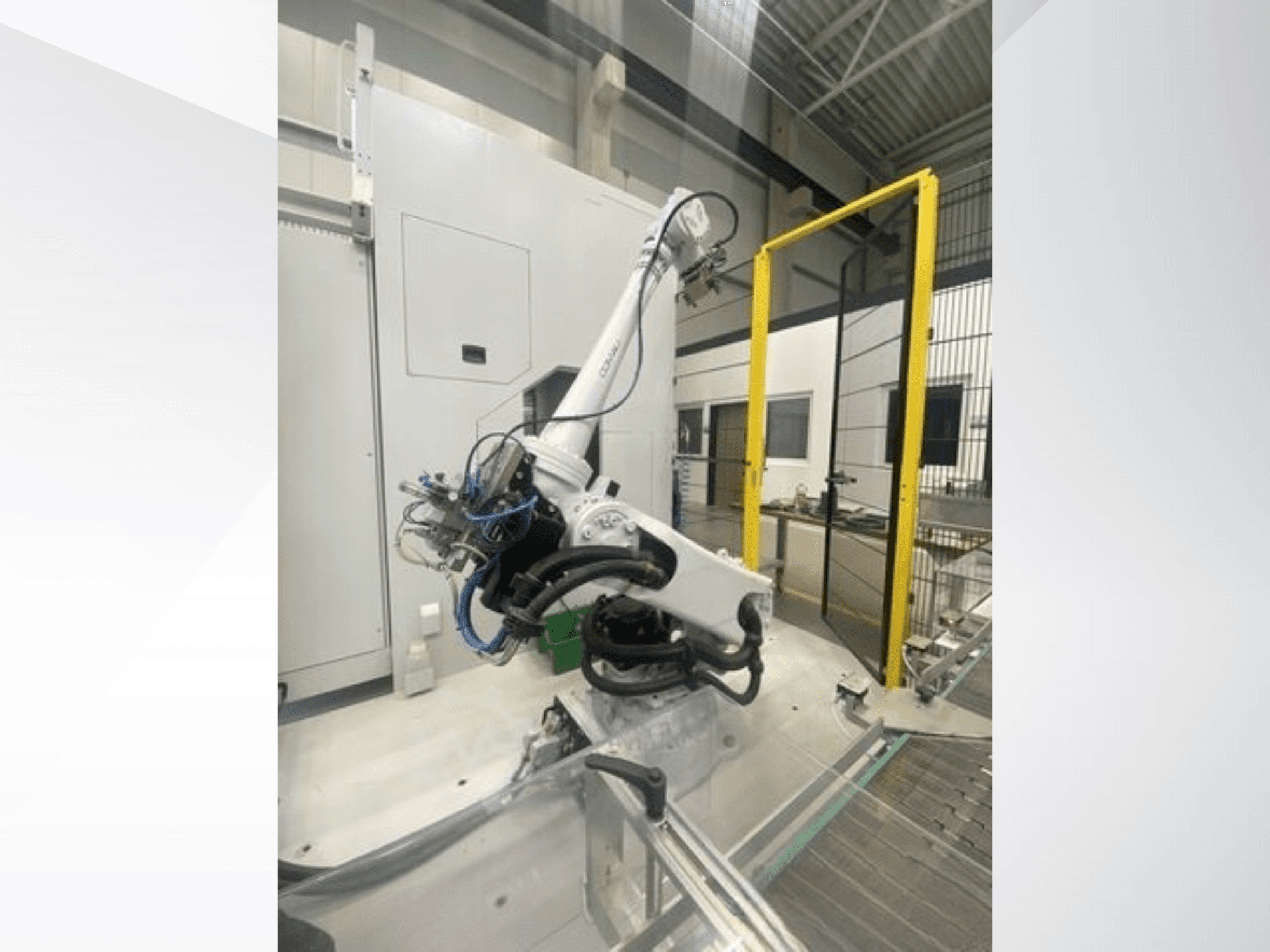 COMAU Smart NJ 40-2.5 roboto rankos vaizdas iš šono, su kabeliais ir geltonais apsauginiais vartais gamykloje.