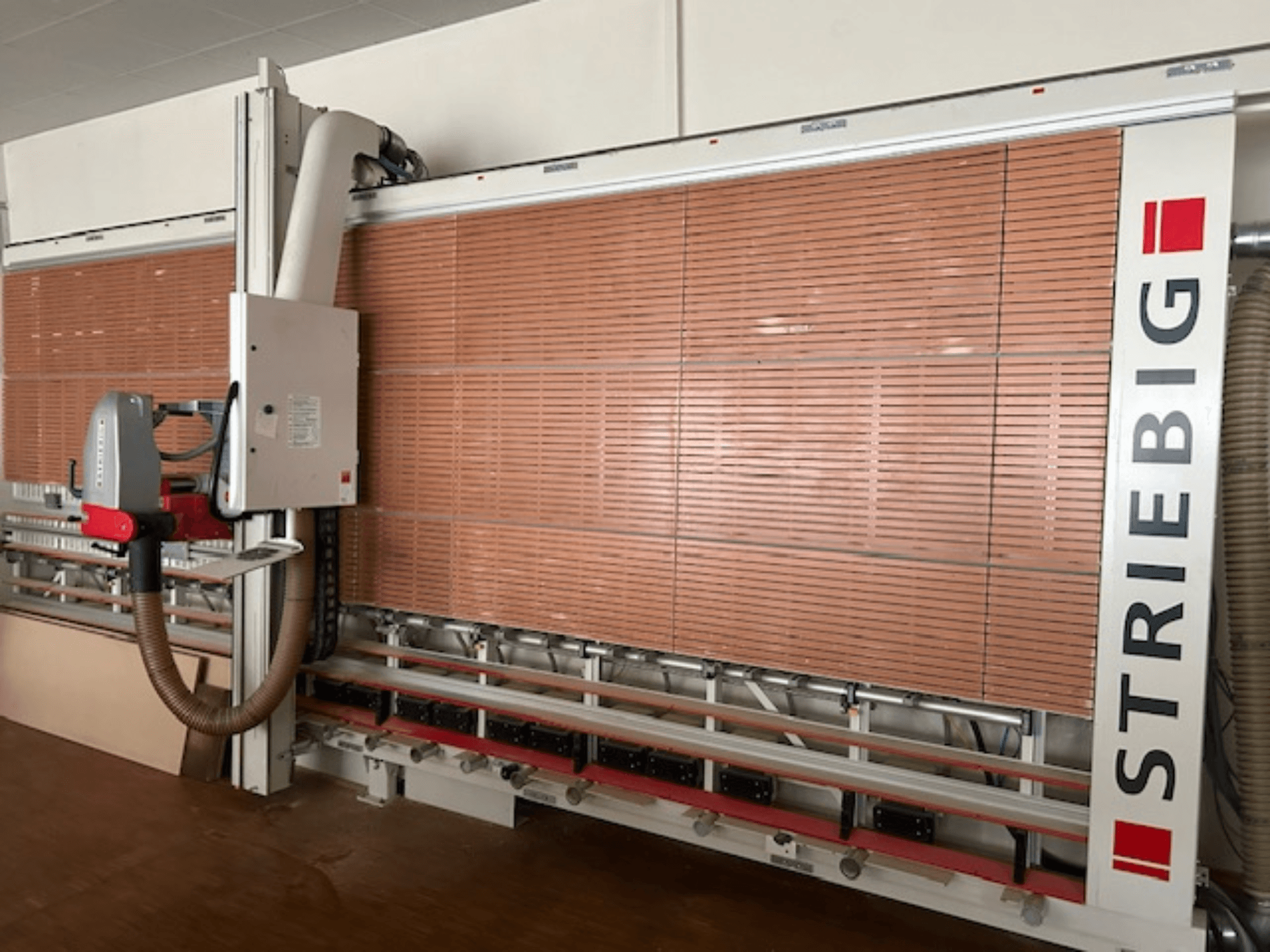 Vertikalaus plokščių pjūklo "Striebig" šoninis vaizdas, kuriame yra motorizuota galvutė, medienos plokščių pjovimo peiliai ir dulkių nusiurbimo sistema.