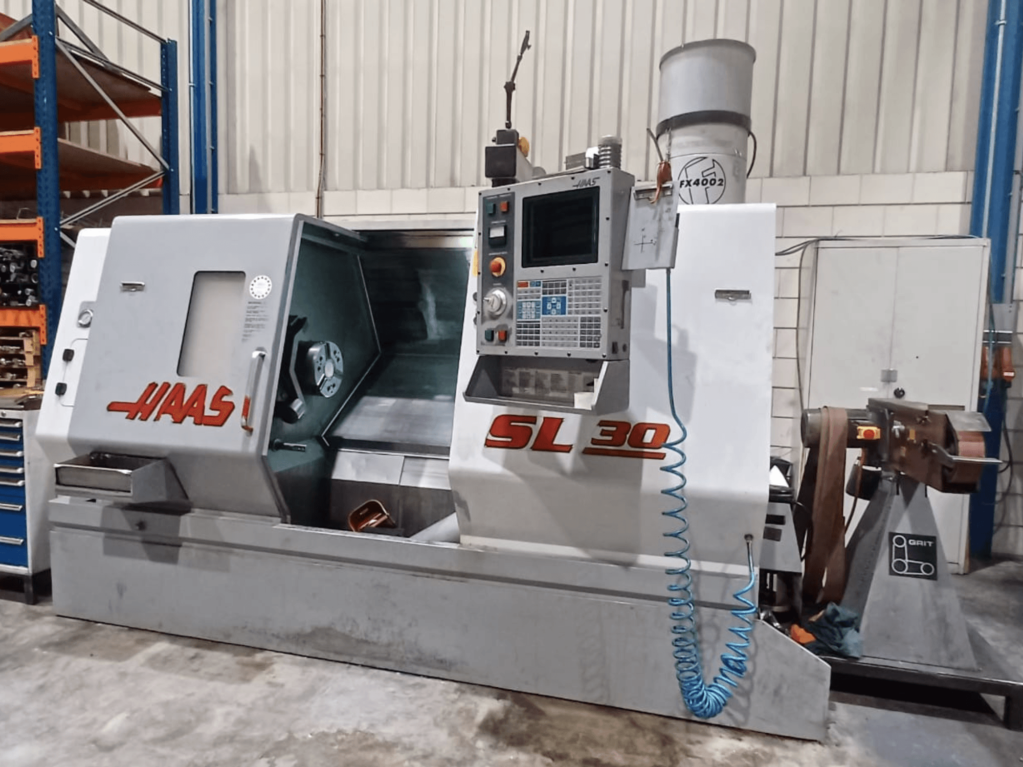 Haas SL 30 CNC tekinimo staklės iš šono, kuriose matomas valdymo skydelis, apdirbimo zona ir integruota aušinimo skysčio sistema, skirta metalo apdirbimui.