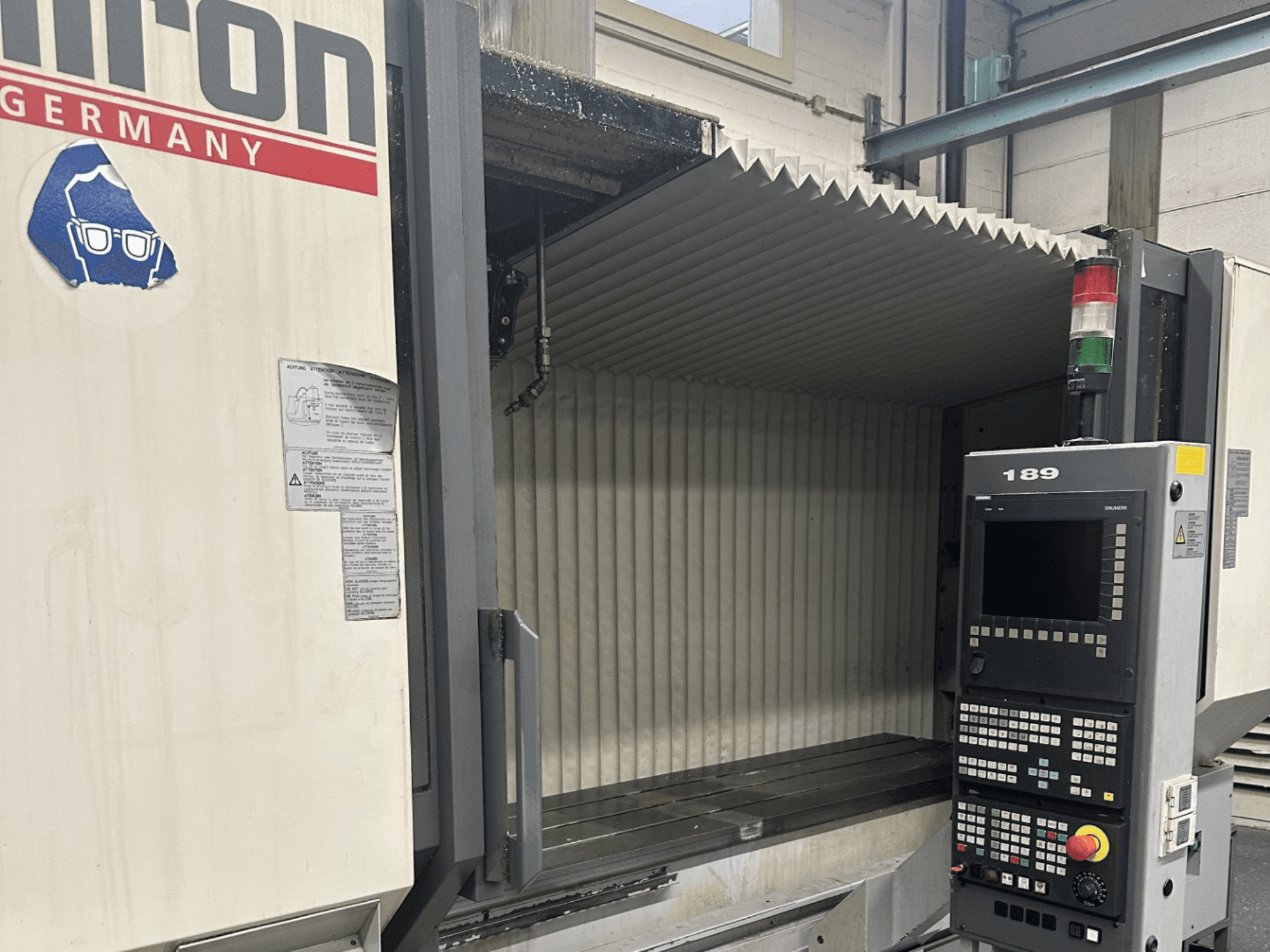 Alt tekstas: Hermle CNC staklių vaizdas iš priekio su valdymo skydeliu, kuriame matomi mygtukai ir ekranas.