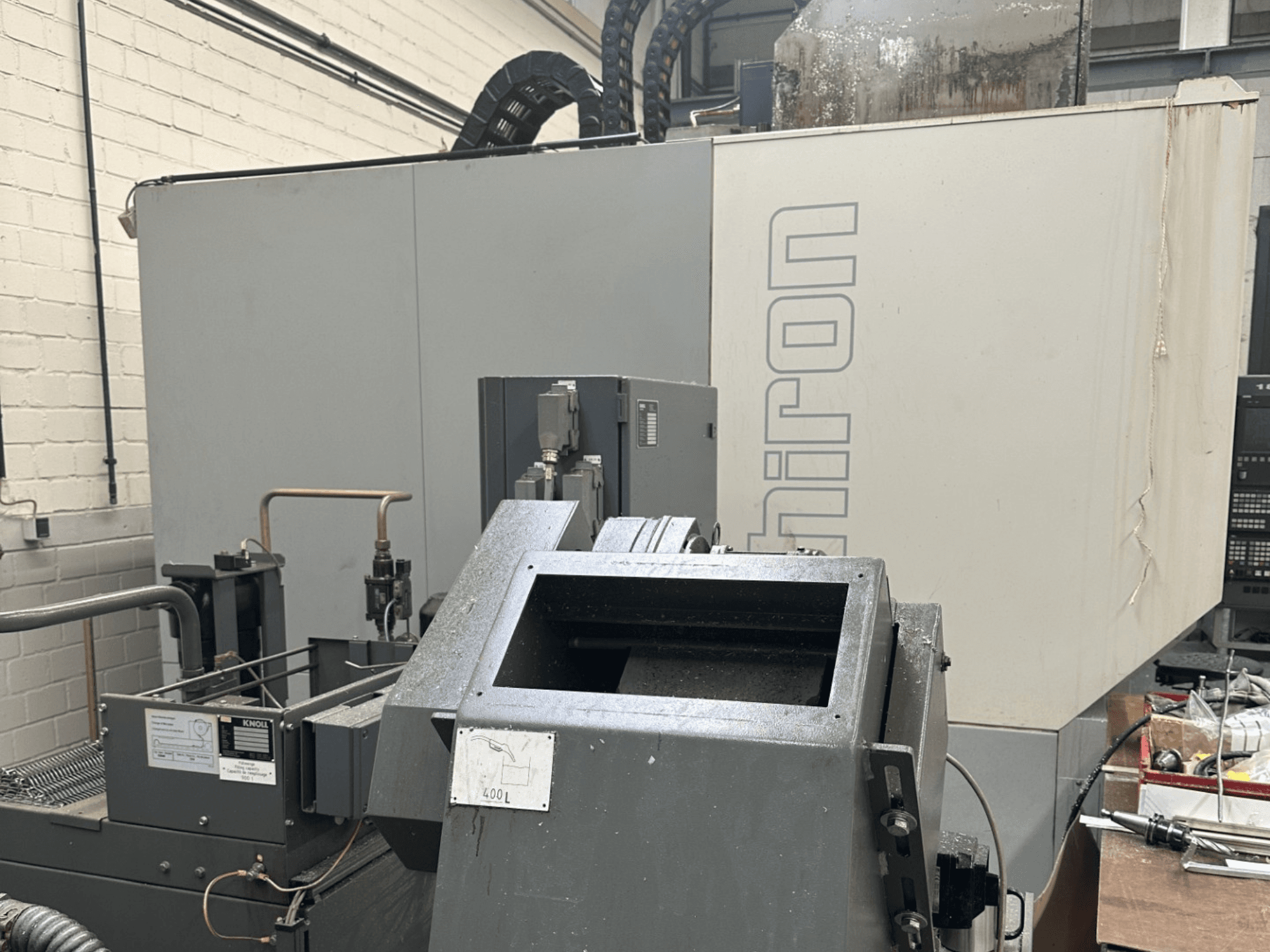 BRAND: Chiron; Pramoninių CNC staklių vaizdas iš priekio, pilka išorė, matomas valdymo skydelis, fokusuojami mašinų komponentai.