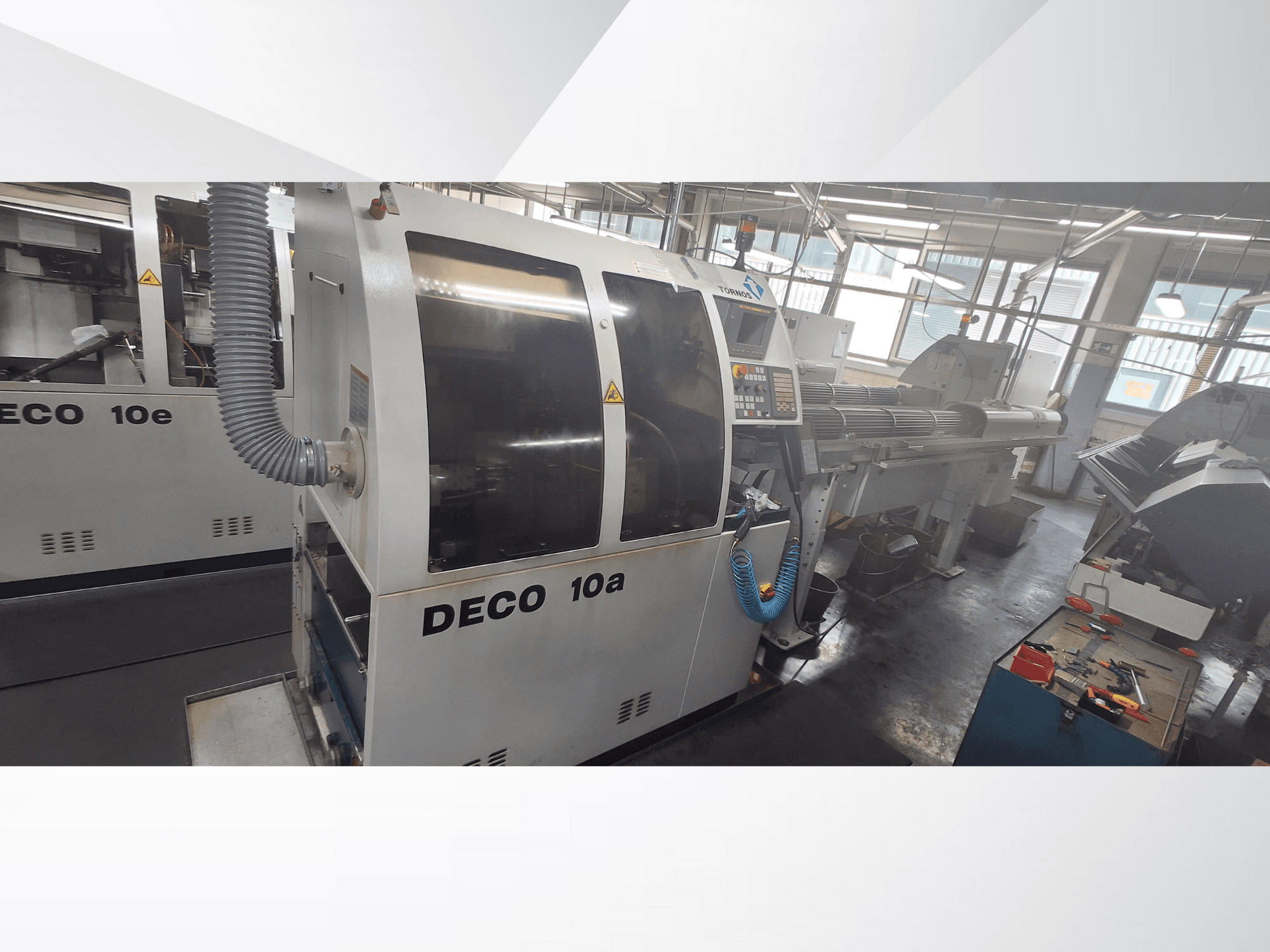 DECO 10a CNC staklės dirbtuvėse, matomas priekinis vaizdas, valdymo skydelis ir išmetimo sistema. Pasižymi tvirta konstrukcija ir tiksliais įrankiais.