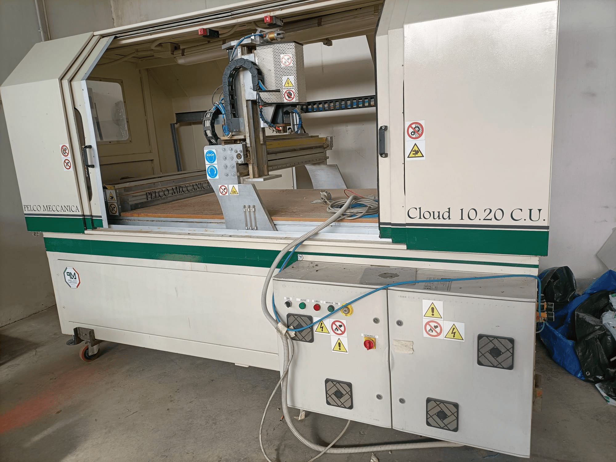 CNC maršrutizatorius MECCANICA CLOUD 10.20 C.U., priekinis vaizdas, kuriame matomas valdymo skydelis ir darbo vieta, matomos saugos etiketės ir žarnos.