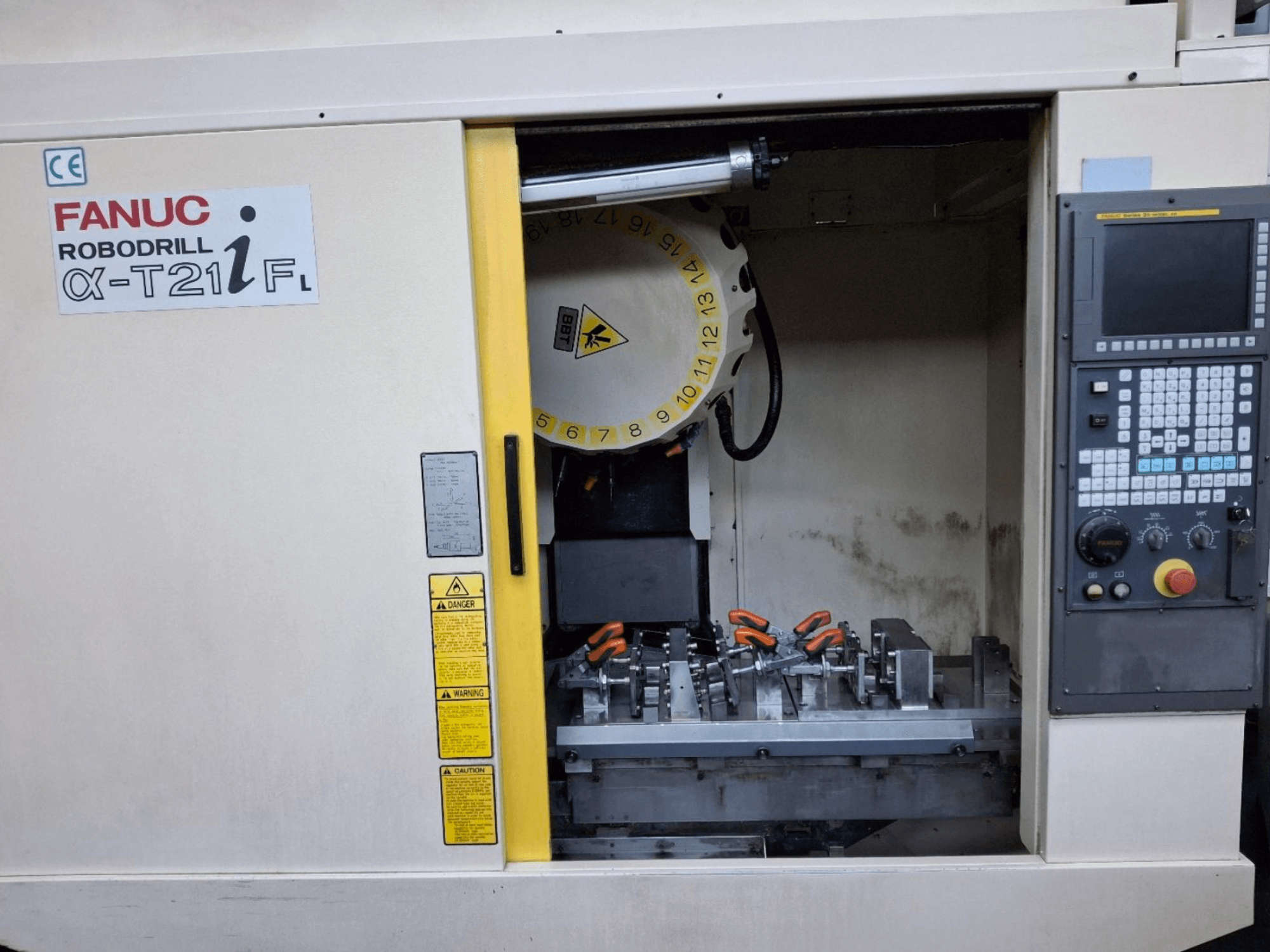 FANUC ROBODRILL α-T21iFL vertikalaus apdirbimo centro priekinis vaizdas, kuriame matomi įrankiai ir valdymo įtaisai staklių spintoje.