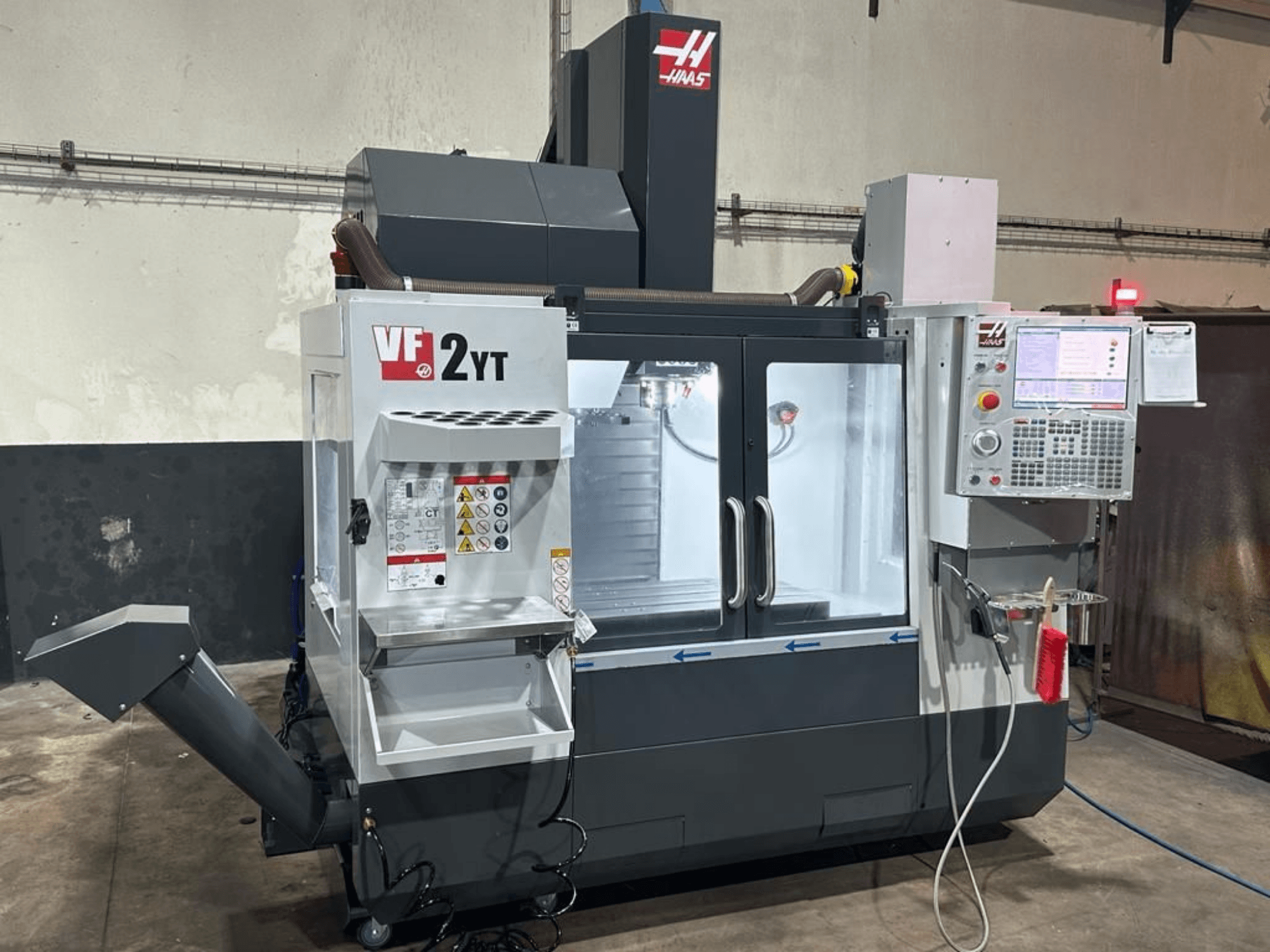 Vertikalusis apdirbimo centras „HAAS VF-2YT-EU“, vaizdas iš priekio, kuriame matomas valdymo pultas ir įrankių laikymo skyrius.