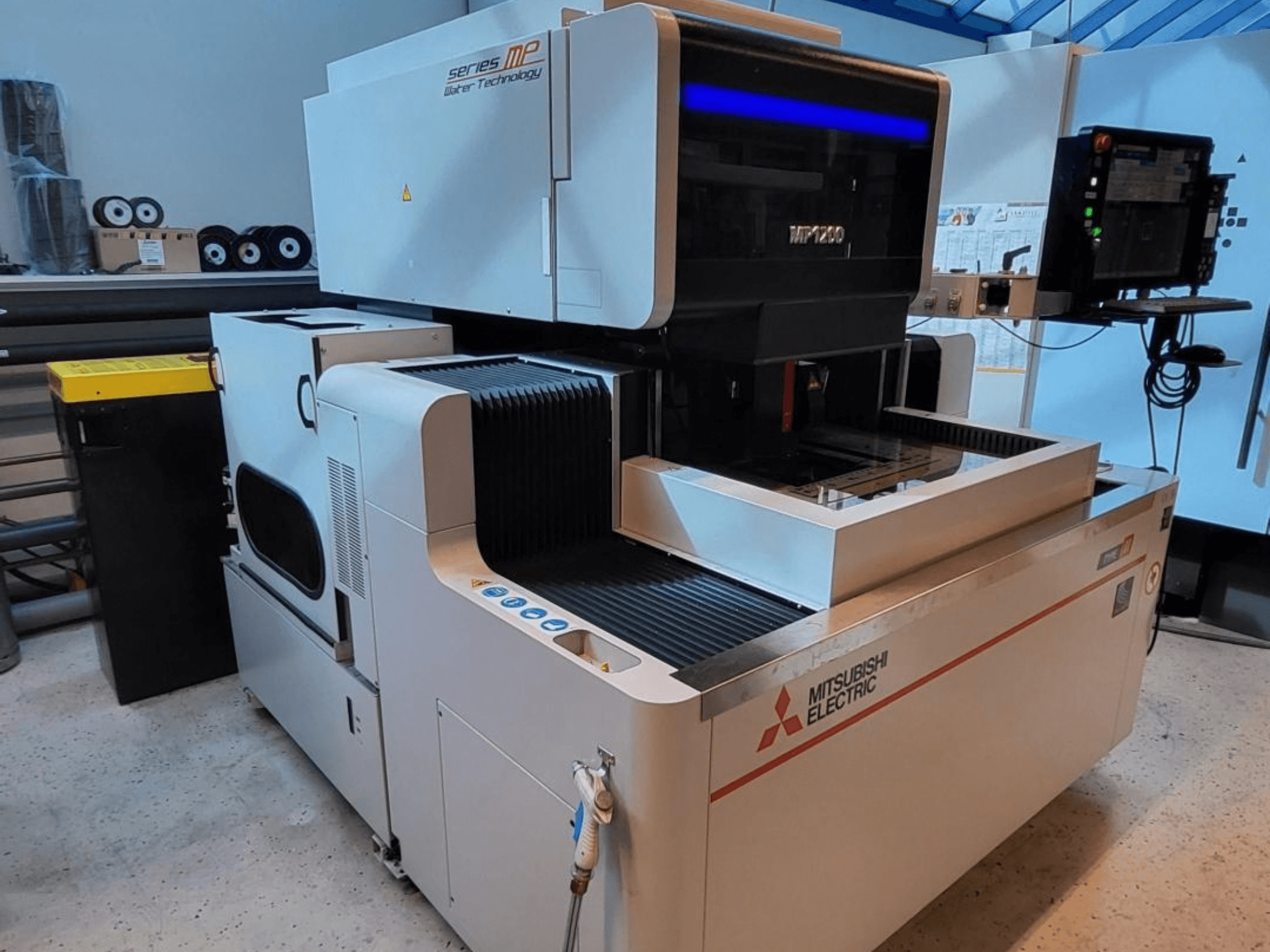 „Mitsubishi MP1200“ vielos elektroerozijos staklės, vaizdas iš priekio, kuriame matomas valdymo pultas, pažangios technologijos detalės ir elegantiškas dizainas.