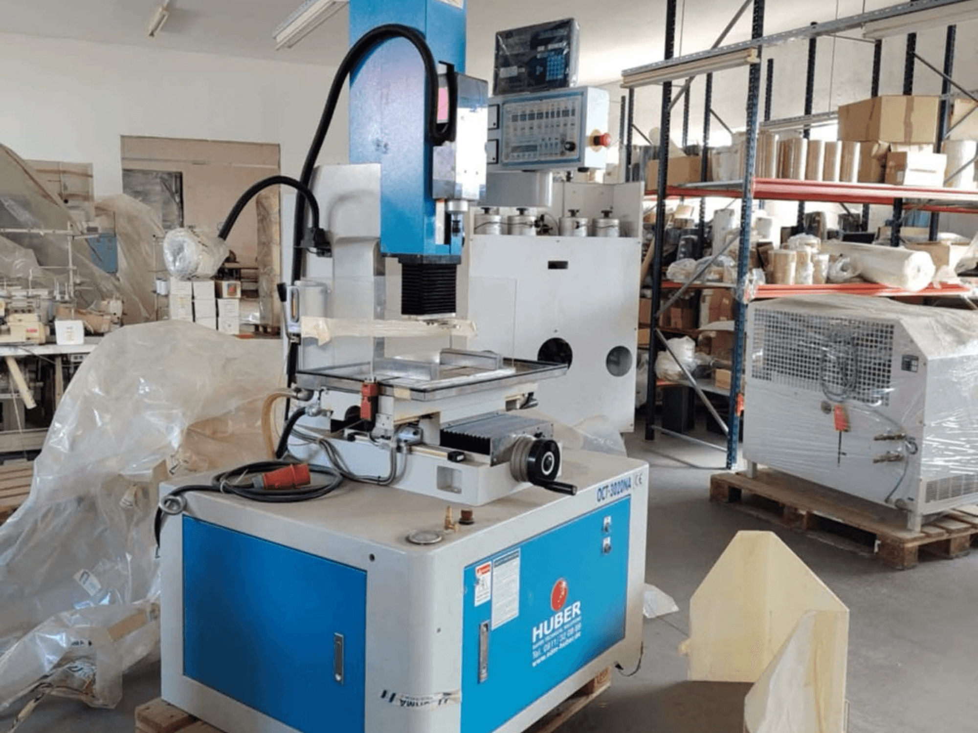 HUBER OCT-3020 NA štampavimo EDM staklės dirbtuvėse, priekinis vaizdas, kuriame matomas mėlynas ir pilkas korpusas, skaitmeniniai valdikliai ir darbo zona.