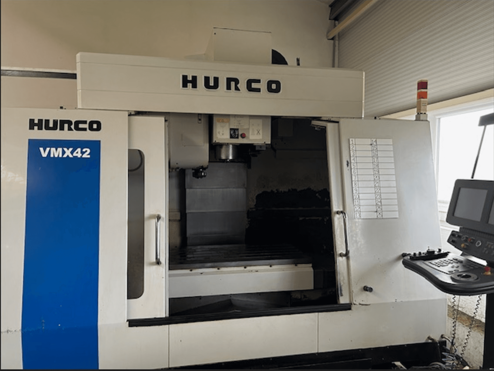 CNC frezavimo staklės "Hurco VMX42 CNC", vaizdas iš priekio, su valdymo skydeliu ir atvira darbo erdve apdirbimo operacijoms.