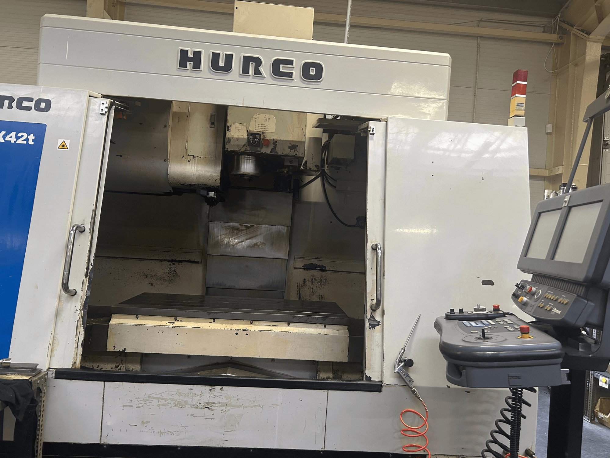 CNC frezavimo staklės "Hurco VMX42T CNC" iš priekio, su atvira darbo erdve ir valdymo skydeliu su mygtukais ir ekranu.