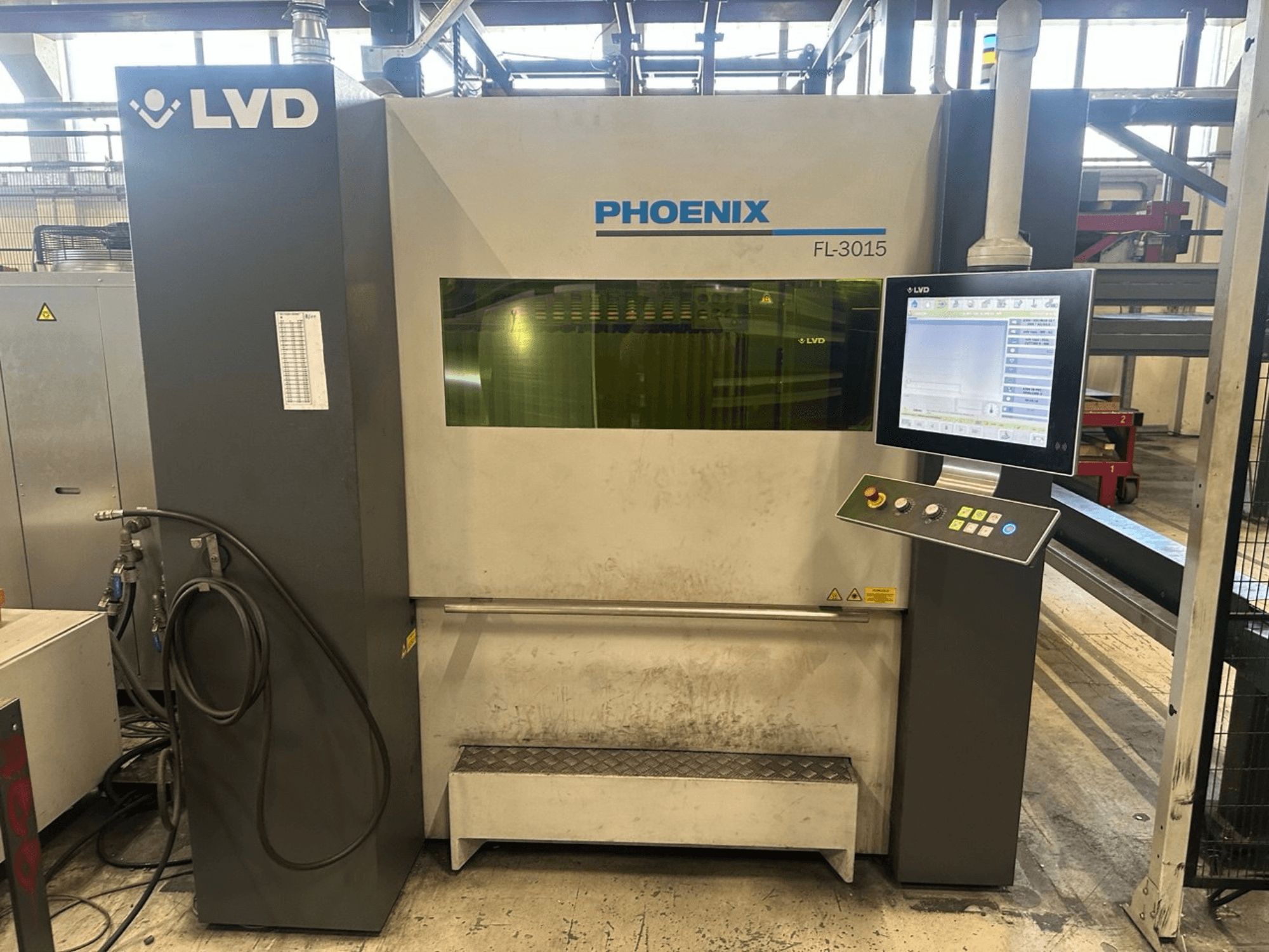 LVD Phoenix FL-3015 lazerinio pjovimo staklės, vaizdas iš priekio, su skaitmeniniu valdymo skydeliu ir matomais vamzdeliais.