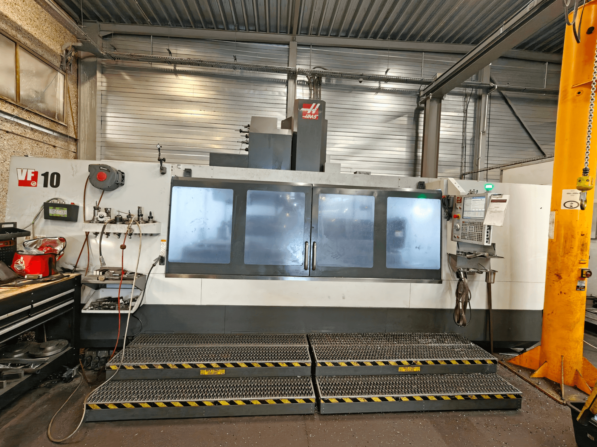 Vertikalus apdirbimo centras „HAAS VF-10/50“, vaizdas iš priekio, su operatoriaus valdymo pultu ir dideliais stebėjimo langais.