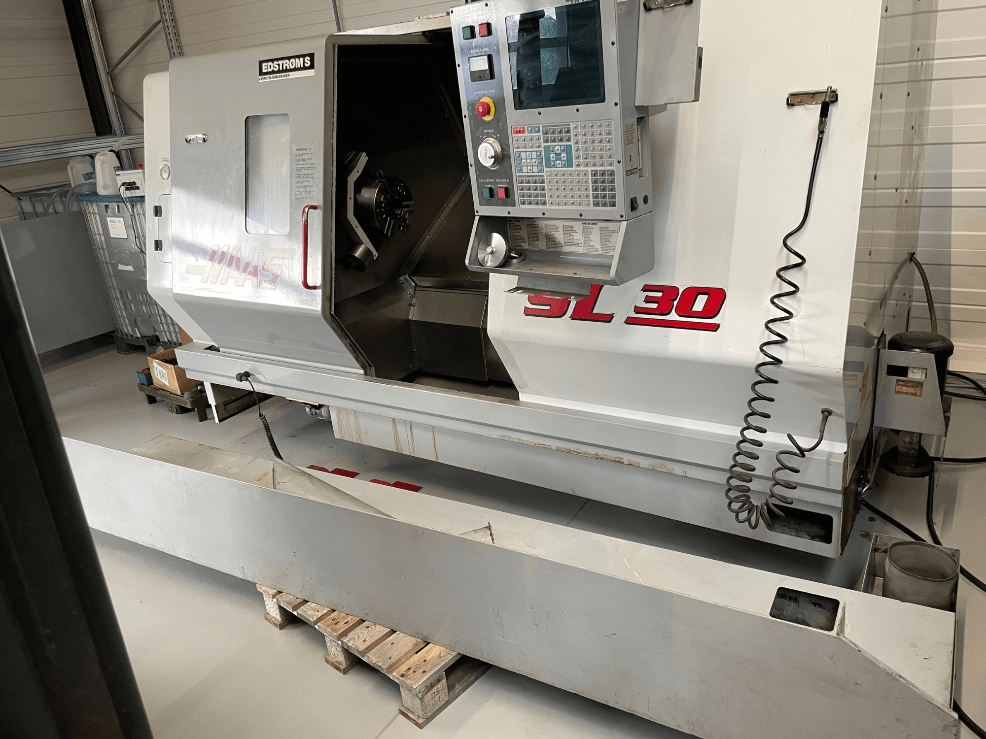 Haas SL 30 CNC tekinimo staklės dirbtuvėse, vaizdas iš šono, su valdymo skydeliu ir atviru sukliu, skirtu apdirbimo užduotims atlikti.