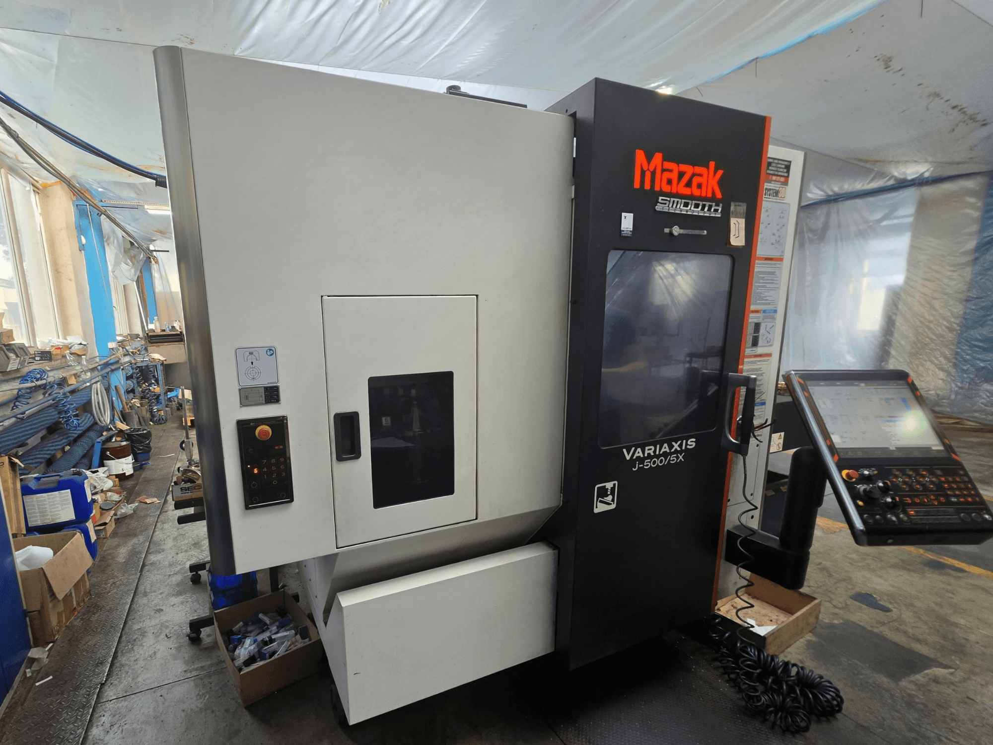 Vertikalusis apdirbimo centras „Mazak VARIAXIS J-500/5X“, šoninis vaizdas, kuriame matomi valdymo elementai ir ekranas, įrengtas dirbtuvėse.