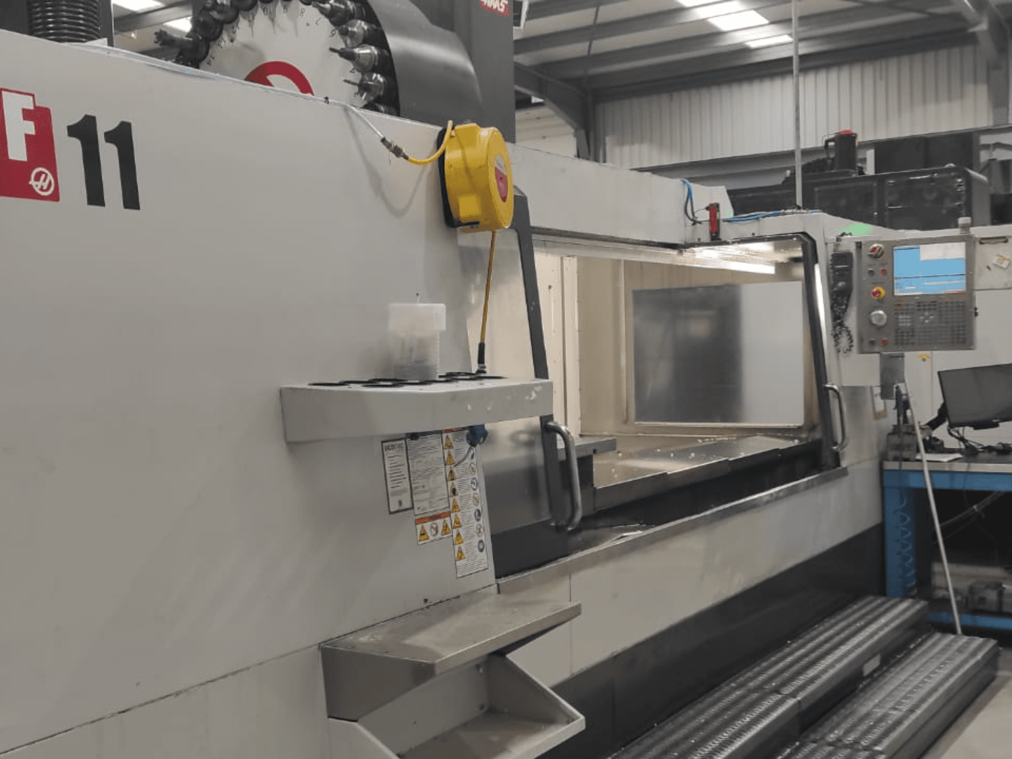 "Haas" mašinos, VF-11 modelis, parodytas iš priekio, matomas valdymo skydelis, didelis darbo plotas ir saugos etiketės.