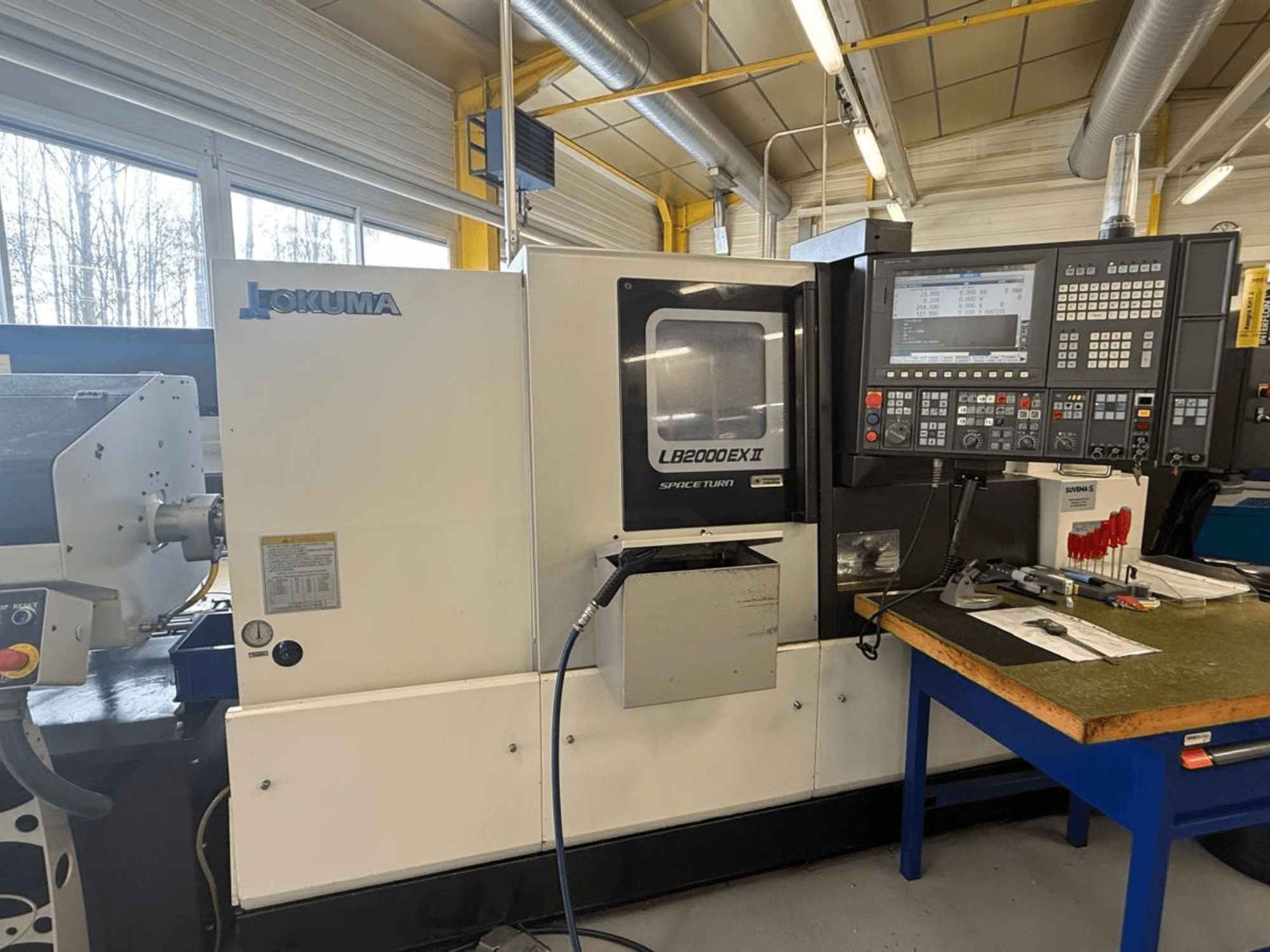 Okuma LB2000EX II horizontalios tekinimo staklės, vaizdas iš priekio; valdymo skydelis, suklio zona ir aplinkinė darbo erdvė.