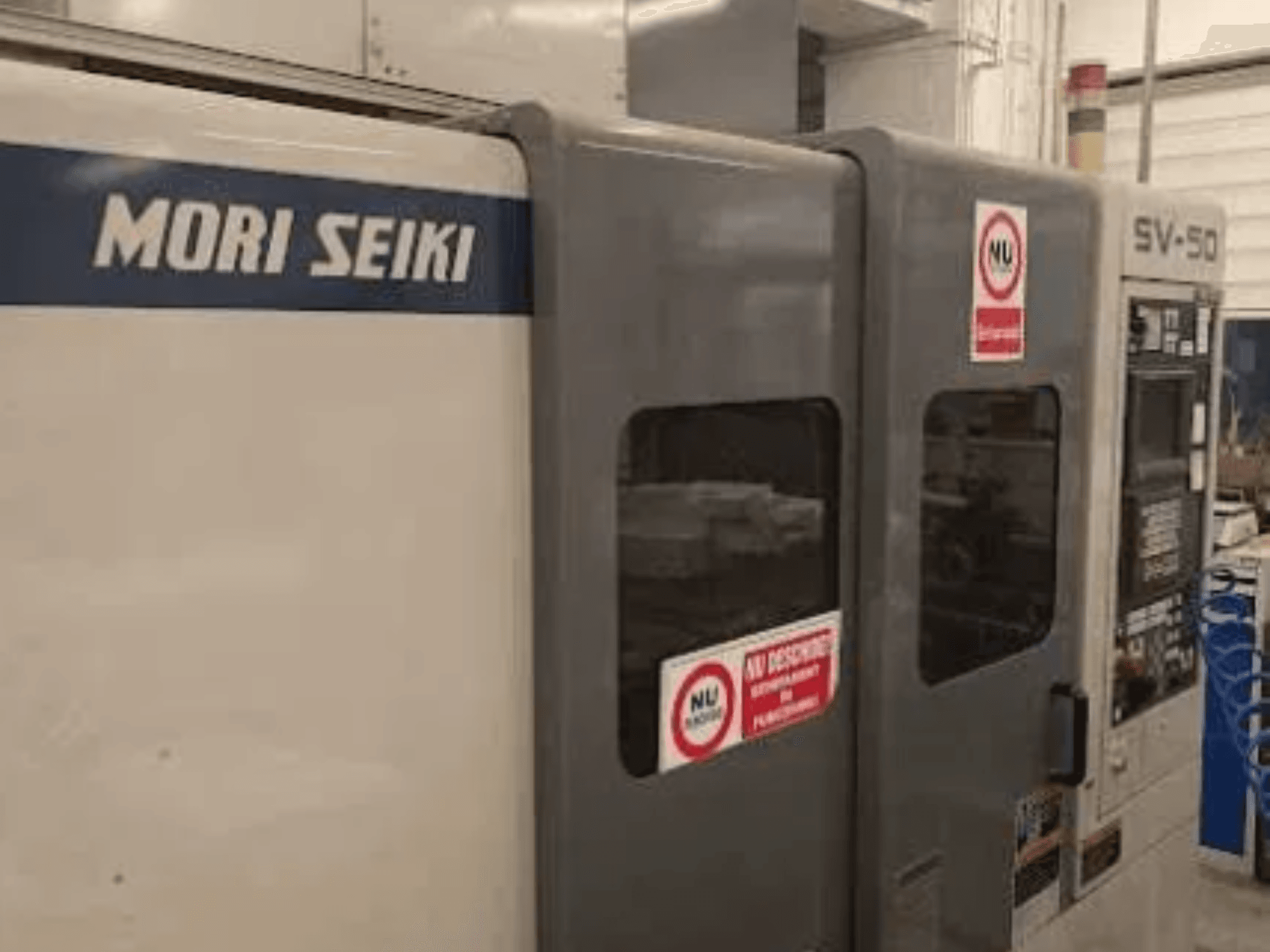 MORI SEIKI SV-50 CNC staklės, vaizdas iš šono; valdymo skydelis ir įspėjamieji saugos lipdukai.