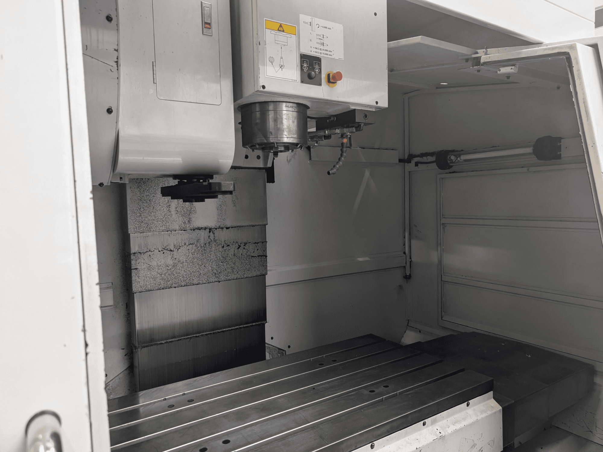 CNC frezavimo staklių su dideliu metaliniu stalu ir suklio varikliu vaizdas iš vidaus, matyti detalūs komponentai ir valdymo skydelis.