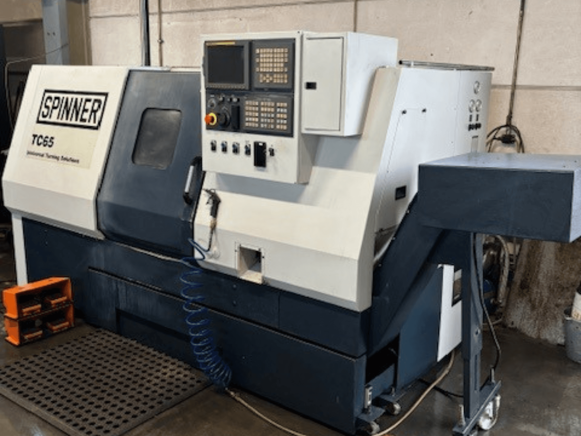 Pramoninių tekinimo staklių "Spinner TC65" vaizdas iš priekio, valdymo skydelis, suspausto oro linija ir įrankių laikymo vieta.