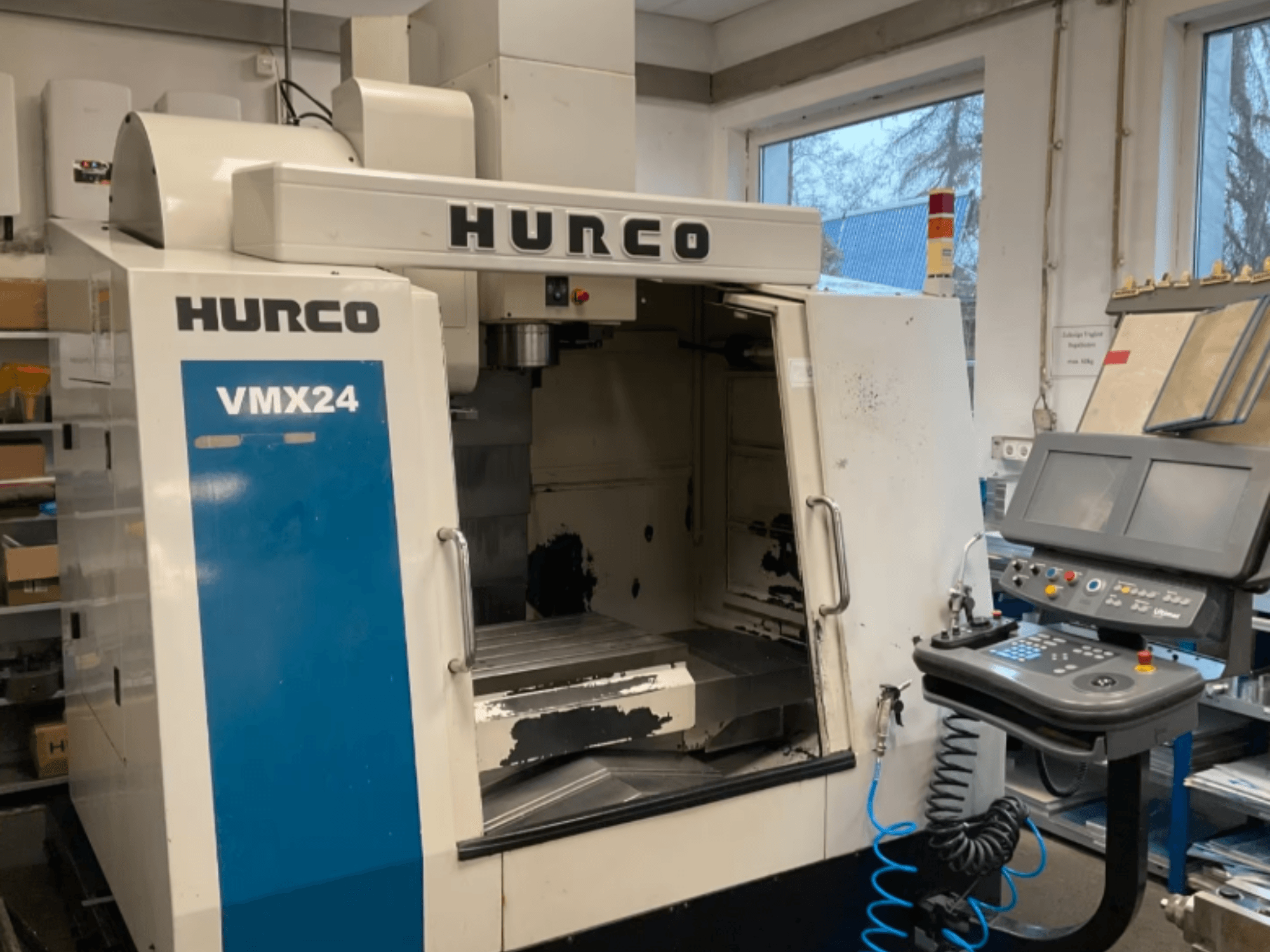 „Hurco VMX24“ vertikalaus apdirbimo centras, vaizdas iš priekio, kuriame matomas valdymo pultas, suklio galvutė ir darbo zona; matyti nedideli nusidėvėjimo požymiai.