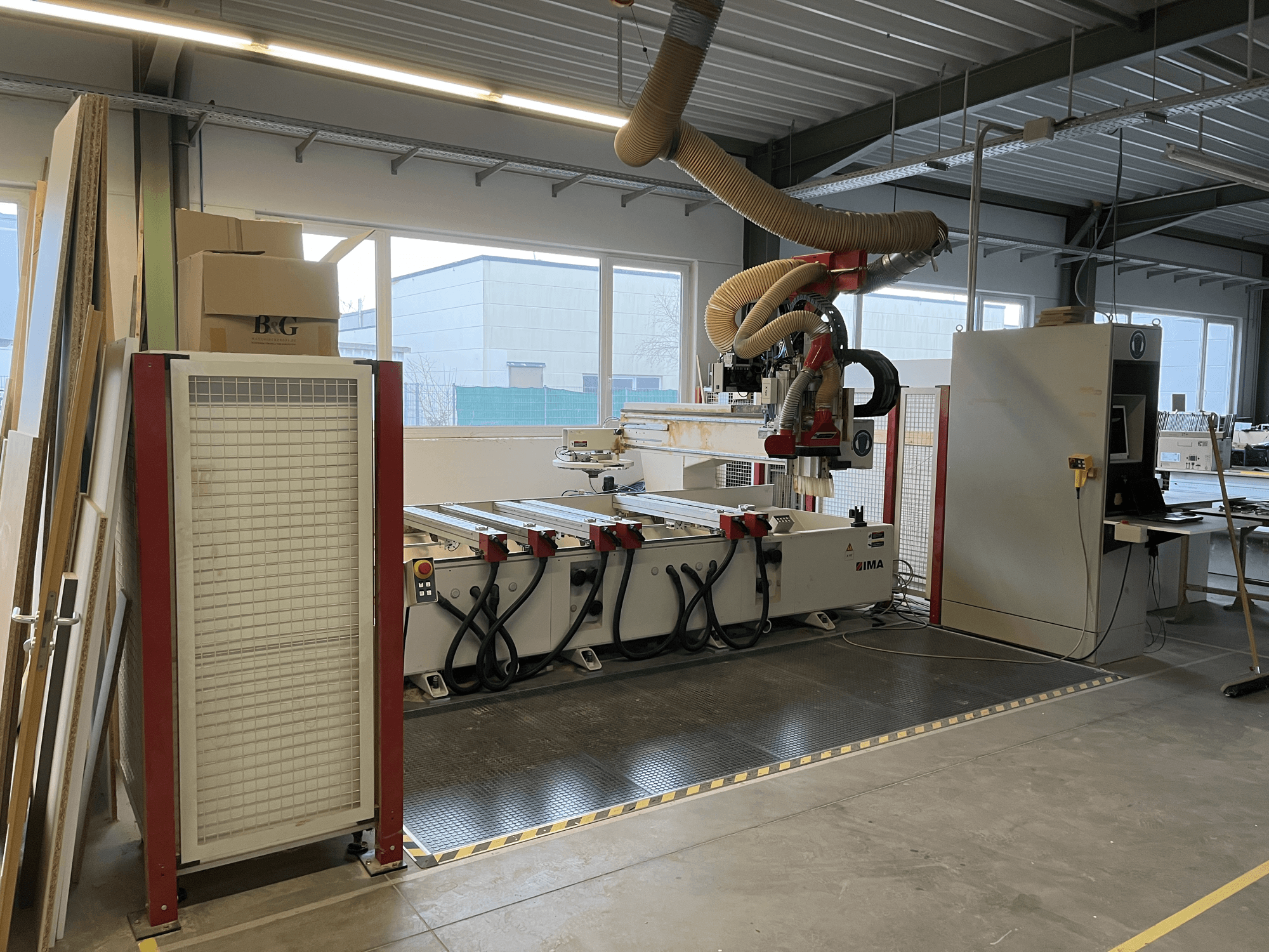 CNC medžio apdirbimo centras IMA BIMA 410 dirbtuvėse, vaizdas iš šono, matomas valdymo skydelis ir dulkių ištraukimo sistema.