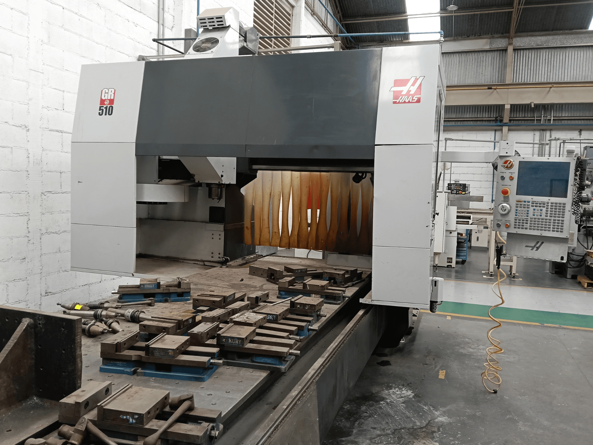 HAAS GR-510 portalinės frezavimo staklių vaizdas iš priekio, kuriame matomas valdymo pultas ir ant stalo esantys apdirbti ruošiniai.