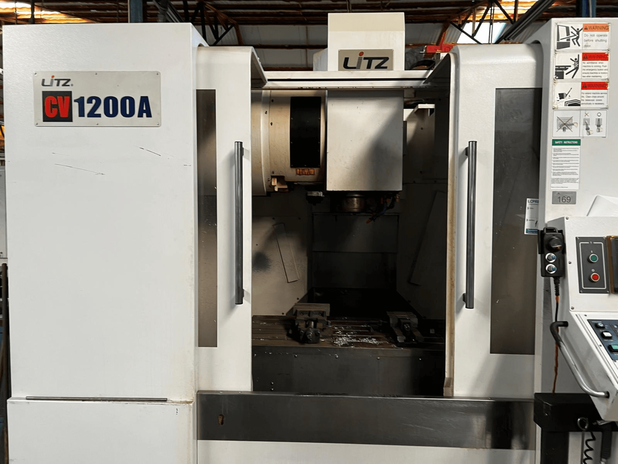 Vertikalus apdirbimo centras „Litz CV1200A“, vaizdas iš priekio, kuriame matomas valdymo pultas, suklis ir atidarytos durys, pro kurias matoma darbo zona.