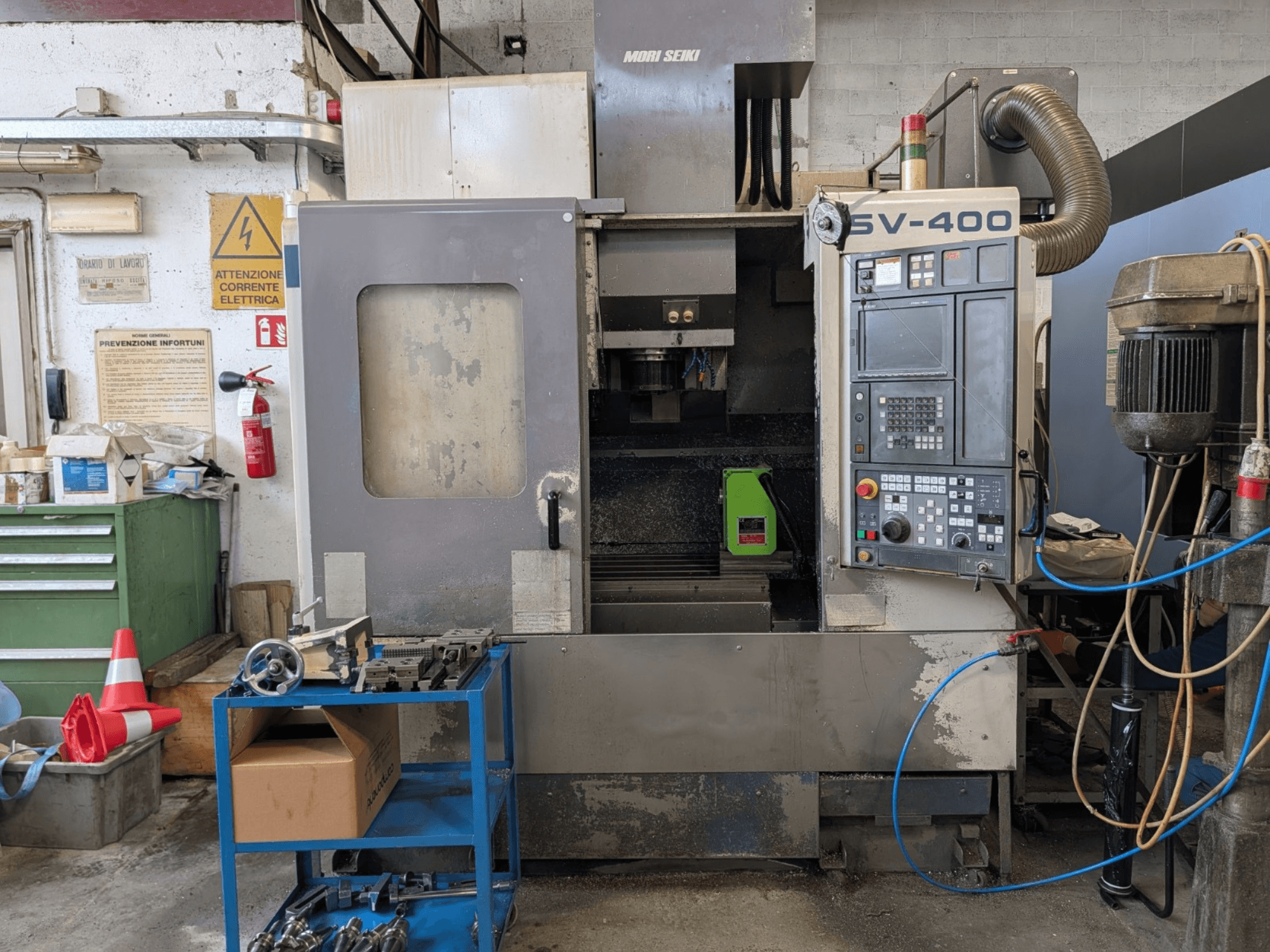 MORI SEIKI SV-400 vertikalusis apdirbimo centras dirbtuvėse, šoninis vaizdas, matomas valdymo skydelis ir šalia esančios staklės.