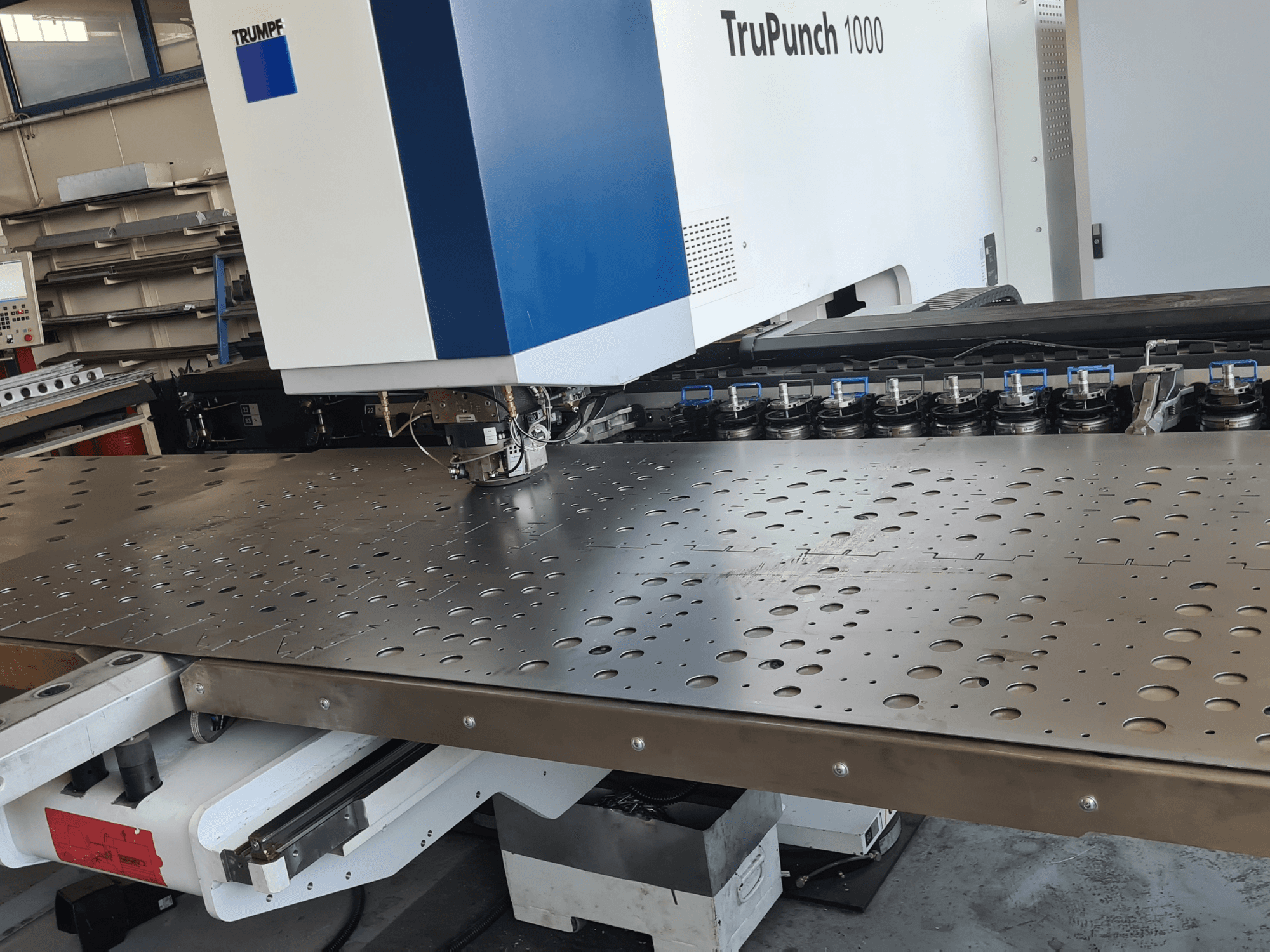 CNC štampavimo staklės „TRUMPF TruPunch 1000“, vaizdas iš priekio, kuriame matomas perforuotas metalinis lakštas ir įrankių konfigūracija.