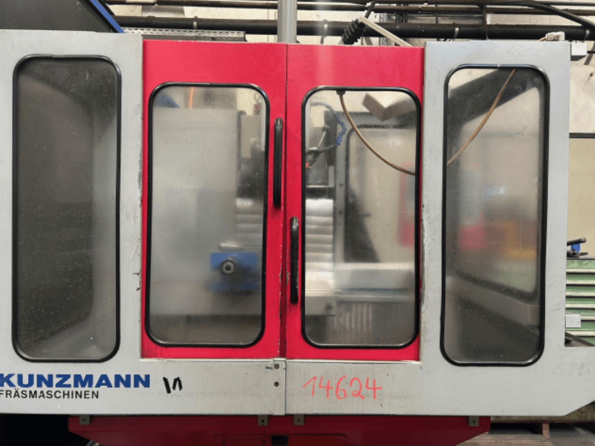 KUNZMANN CNC staklių vaizdas iš priekio, raudonos ir pilkos spalvos skydai, viduje matomas valdymo skydelis ir įrankių laikiklis.