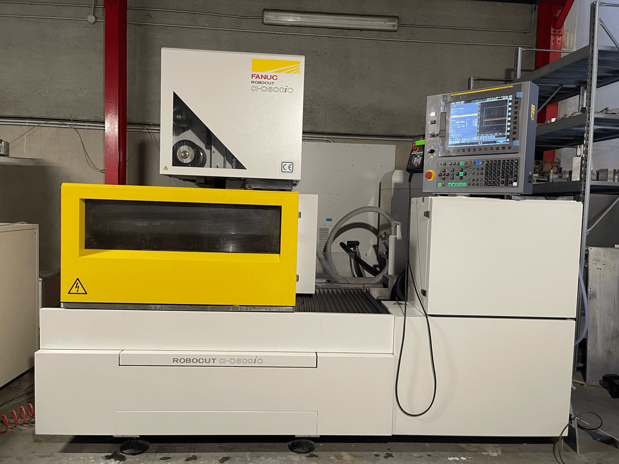 FANUC Robocut α-C600iC, šoninis CNC staklių vaizdas su geltonu apsauginiu gaubtu ir valdymo skydeliu, demonstruojantis tikslaus pjovimo galimybes.