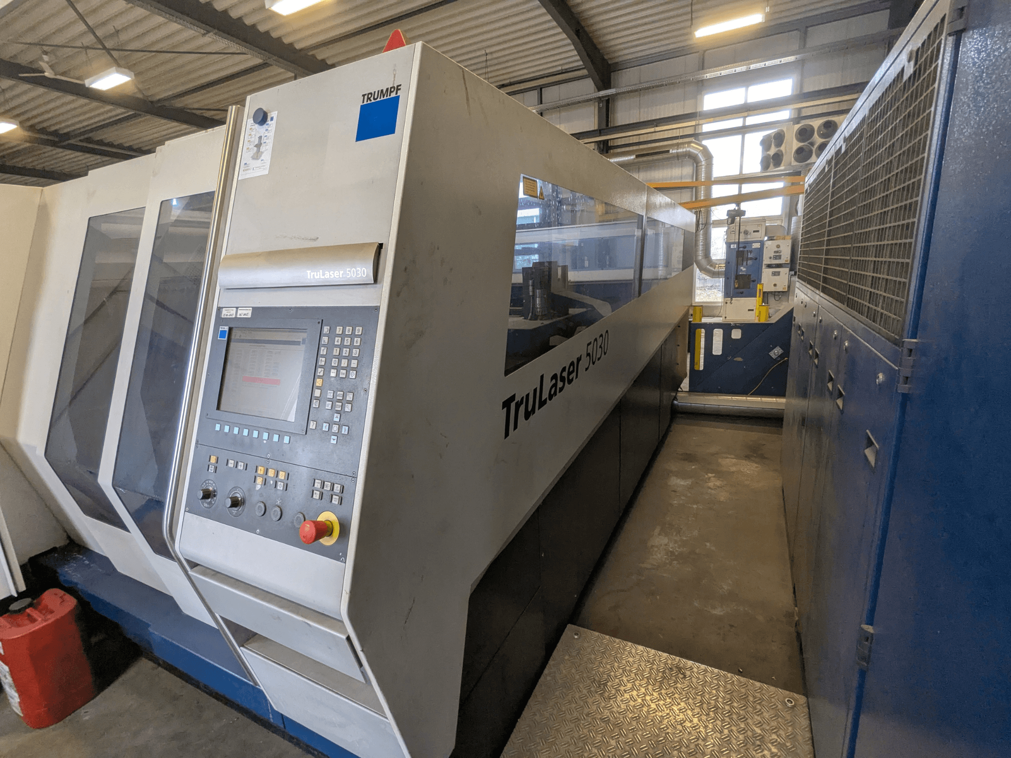 TRUMPF TruLaser 5030 CO2 lazerinio pjovimo staklės, priekinis vaizdas, kuriame matomas valdymo skydelis ir aptakus dizainas, pramoninėje aplinkoje.