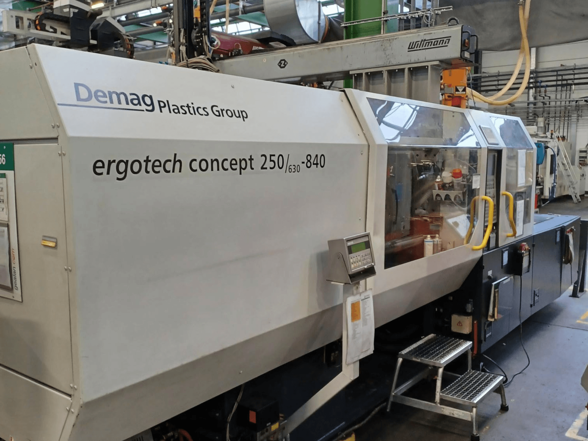 "Demag ergotech concept 250/630-840" liejimo mašinos, vaizdas iš priekio, matyti skaitmeniniai valdikliai ir skaidrūs apsauginiai dangteliai.