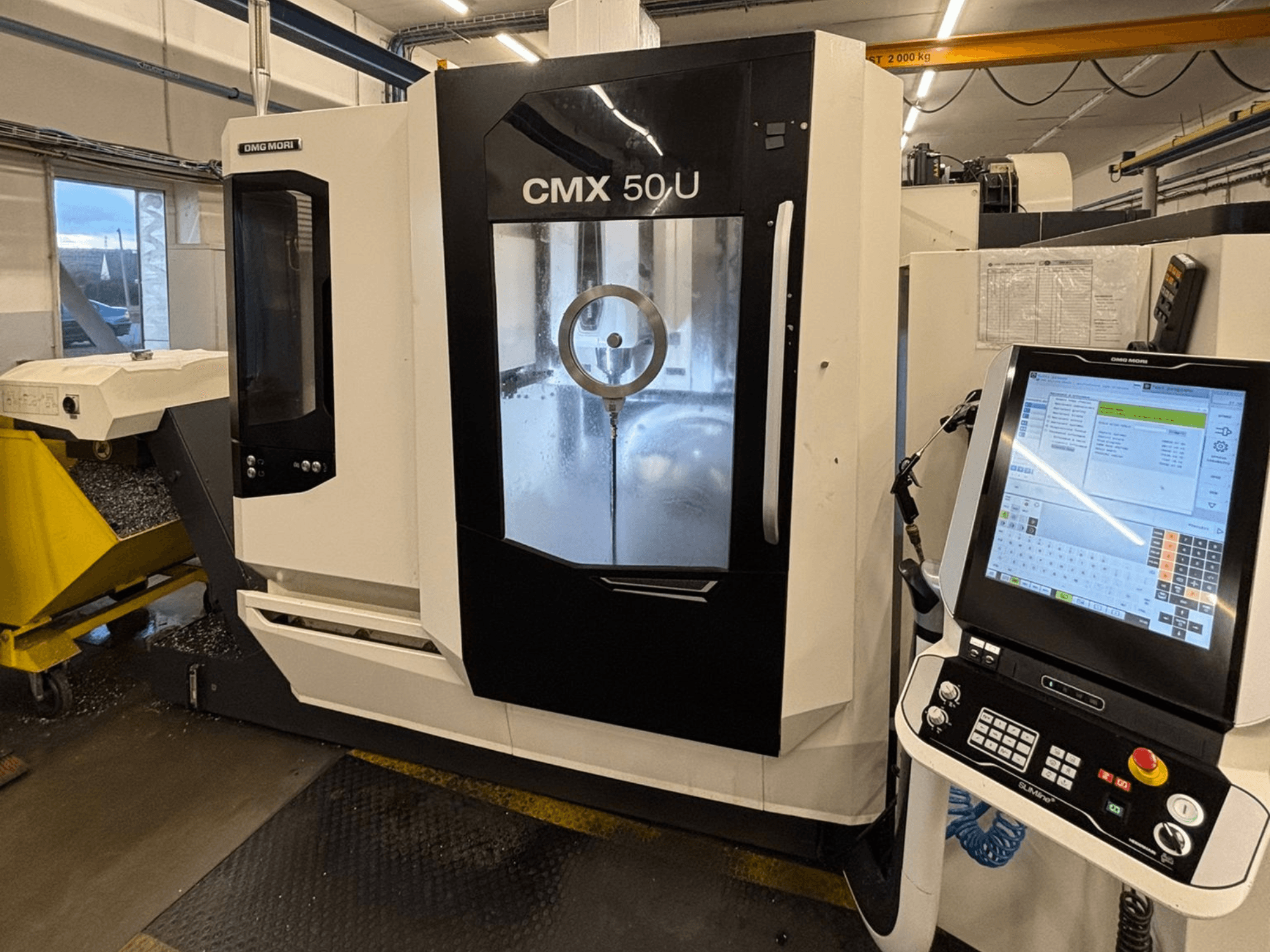 DMG MORI CMX 50 U vertikalusis apdirbimo centras, vaizdas iš priekio su valdymo skydeliu ir stikliniu ekranu, kuriame matoma vidinė mechanika.