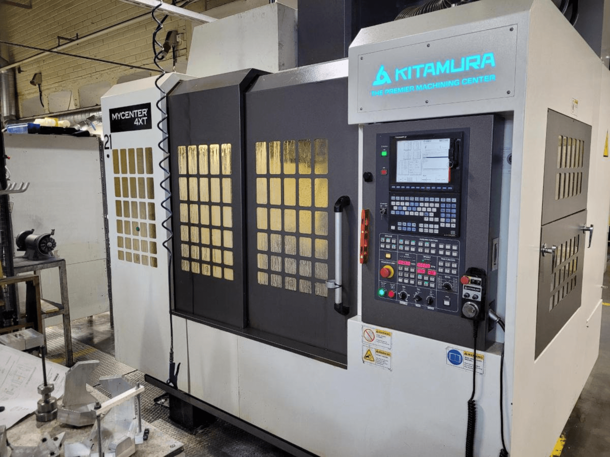 Vertikalus "Kitamura Mycenter-4XT" apdirbimo centro vaizdas su valdymo skydeliu ir šviečiančiu prekės ženklu.