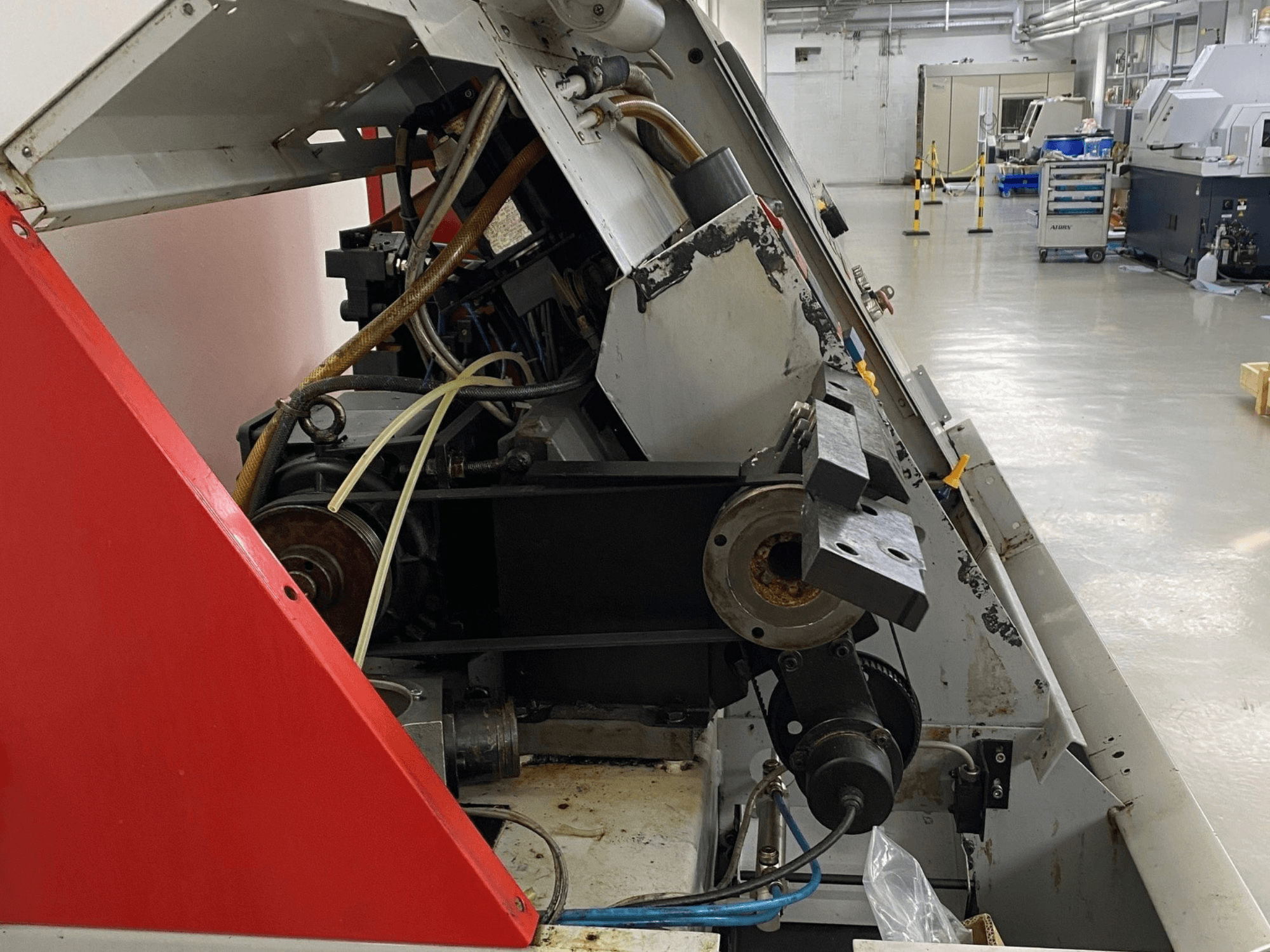 EMCO Emcoturn 325 horizontaliojo tekinimo staklės, šoninis vaizdas, rodantis pavaros komponentus ir hidrauliką pramoninėje aplinkoje.