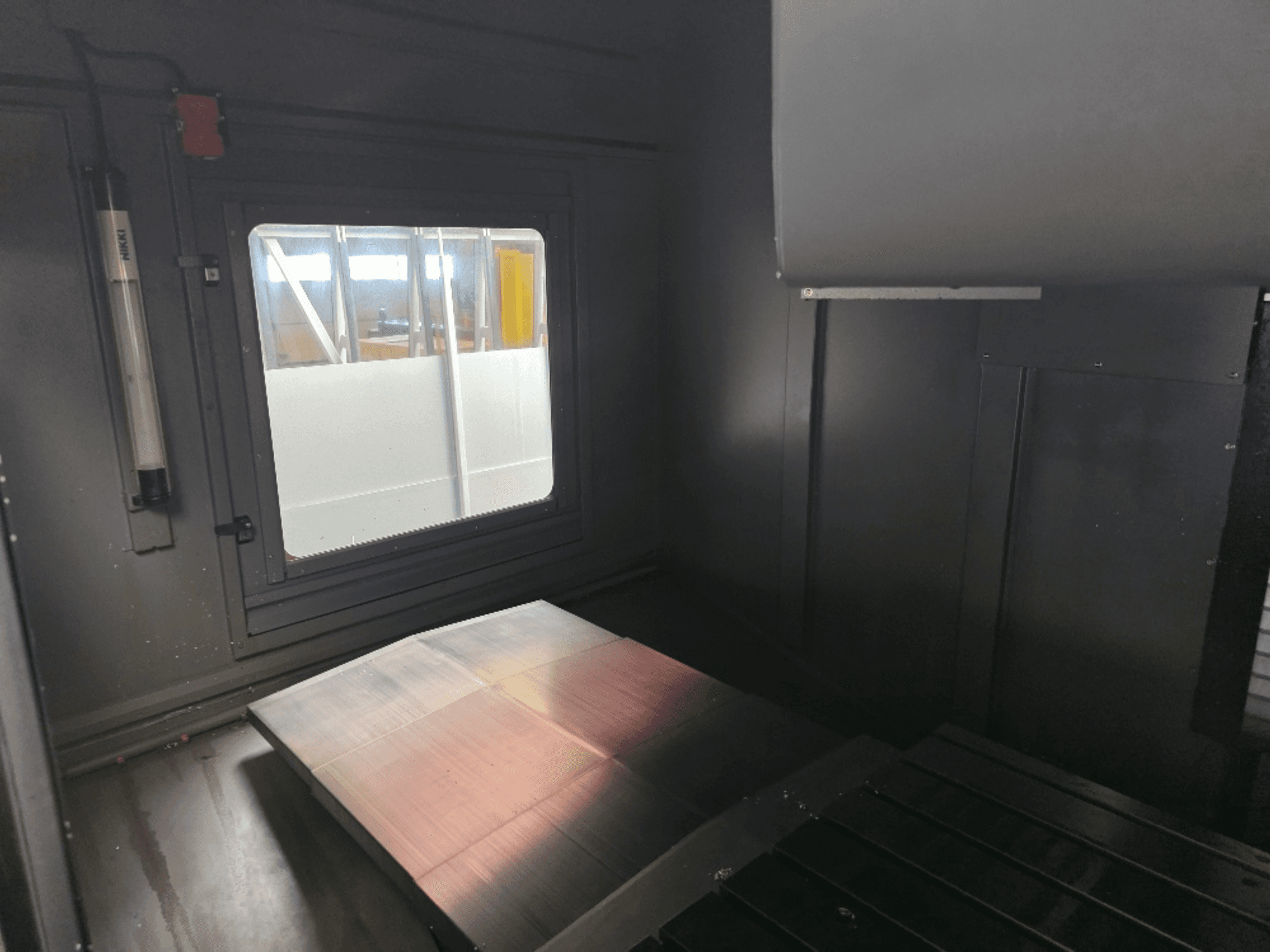 Mašinos korpuso su poliruoto metalo plokšte, šoniniu langu ir minimaliu apšvietimu vidaus vaizdas. Prekės ženklo nematyti.