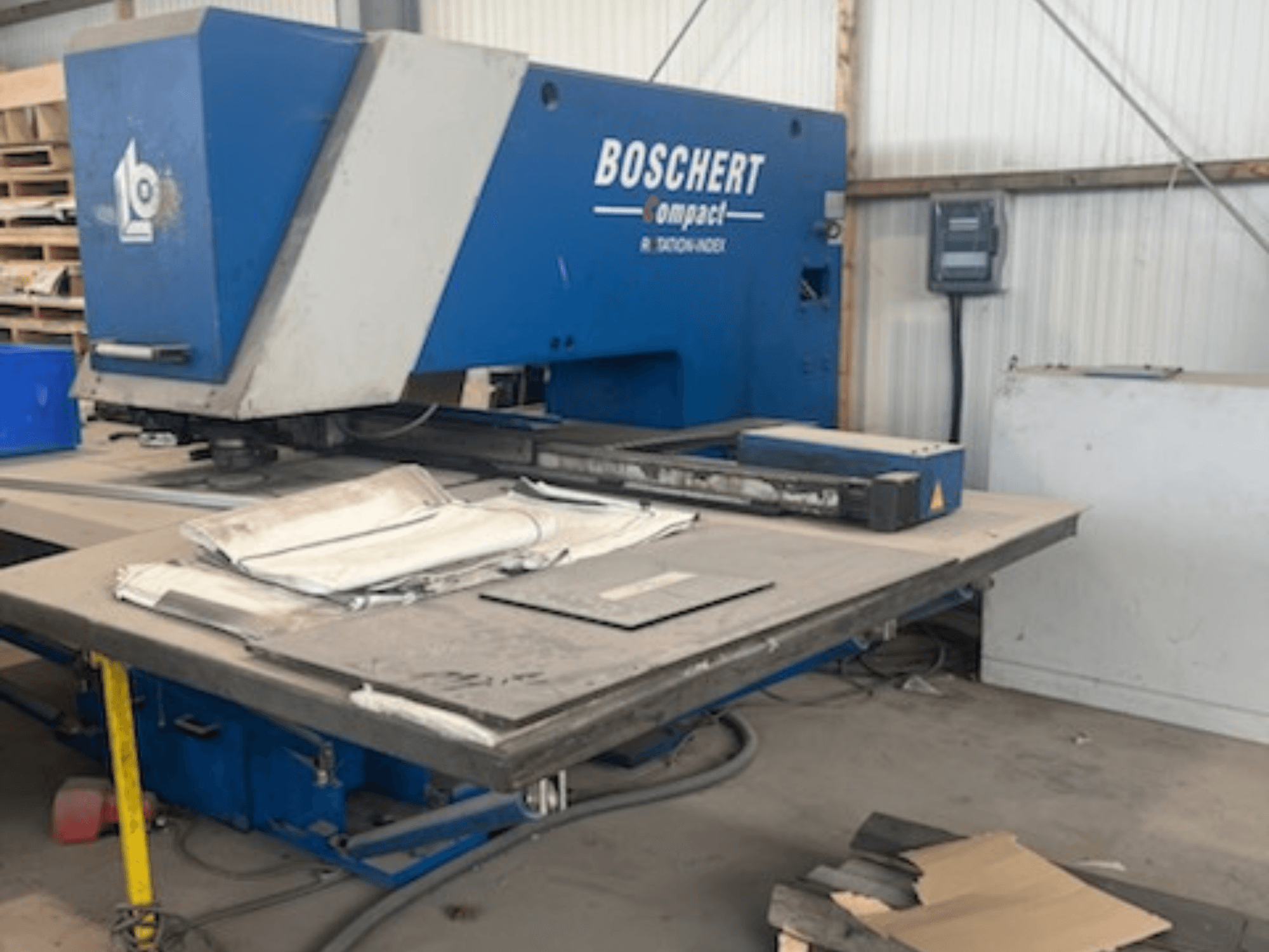 „BOSCHERT COMPACT 1000“ CNC štampavimo staklės dirbtuvėse; nuotraukoje matomas priekinis vaizdas su ant stalo padėtais metaliniais lakštais.