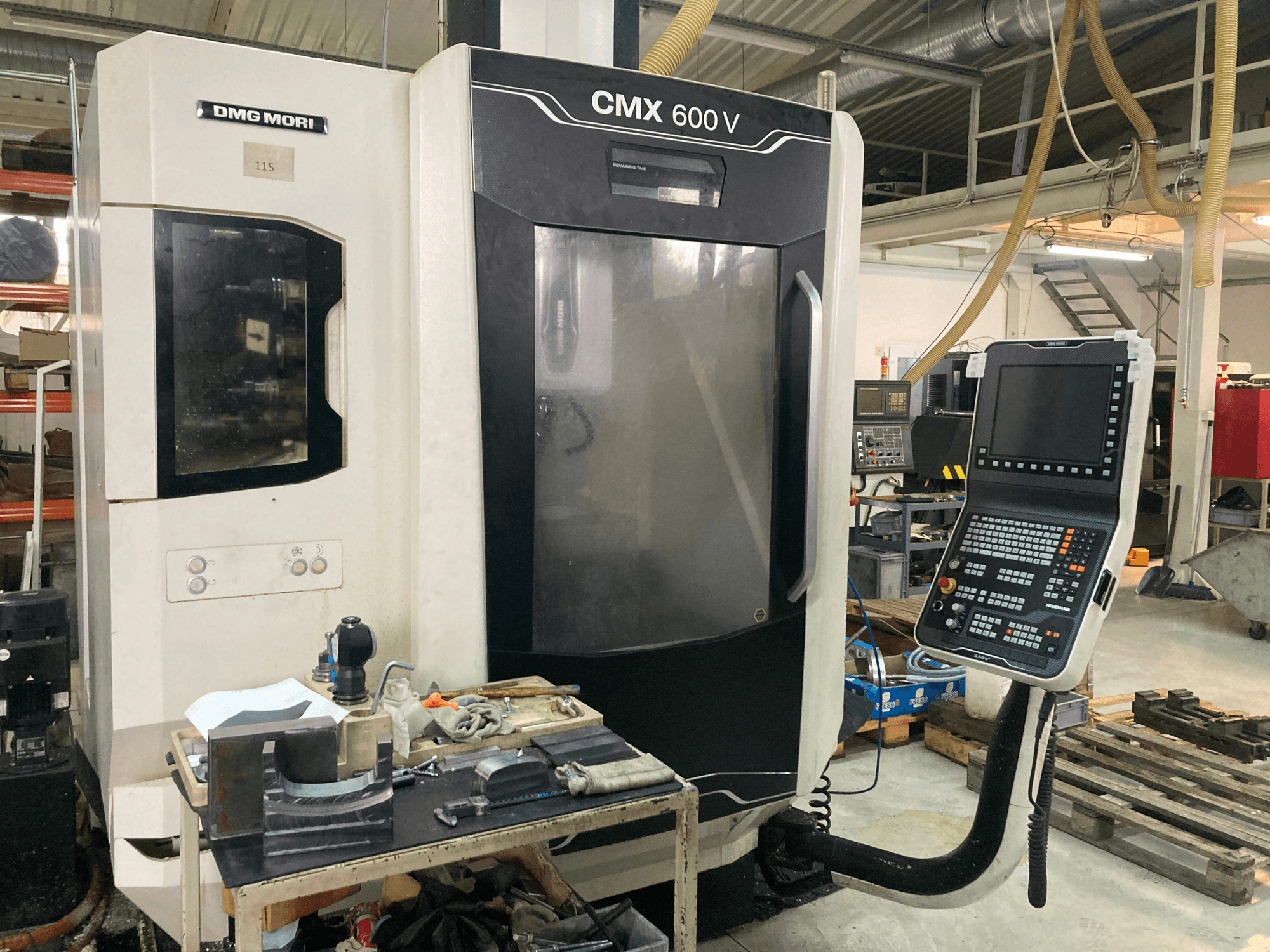 DMG MORI CMX 600 V frezavimo staklės, žiūrint iš priekio, matyti valdymo skydelis ir stalas su įrankiais.