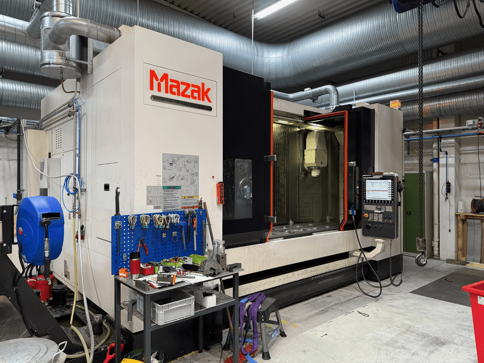 "Mazak" CNC staklės iš priekio, kuriose matomi valdymo elementai, įrankiai ir darbo vieta apdirbimo aplinkoje.