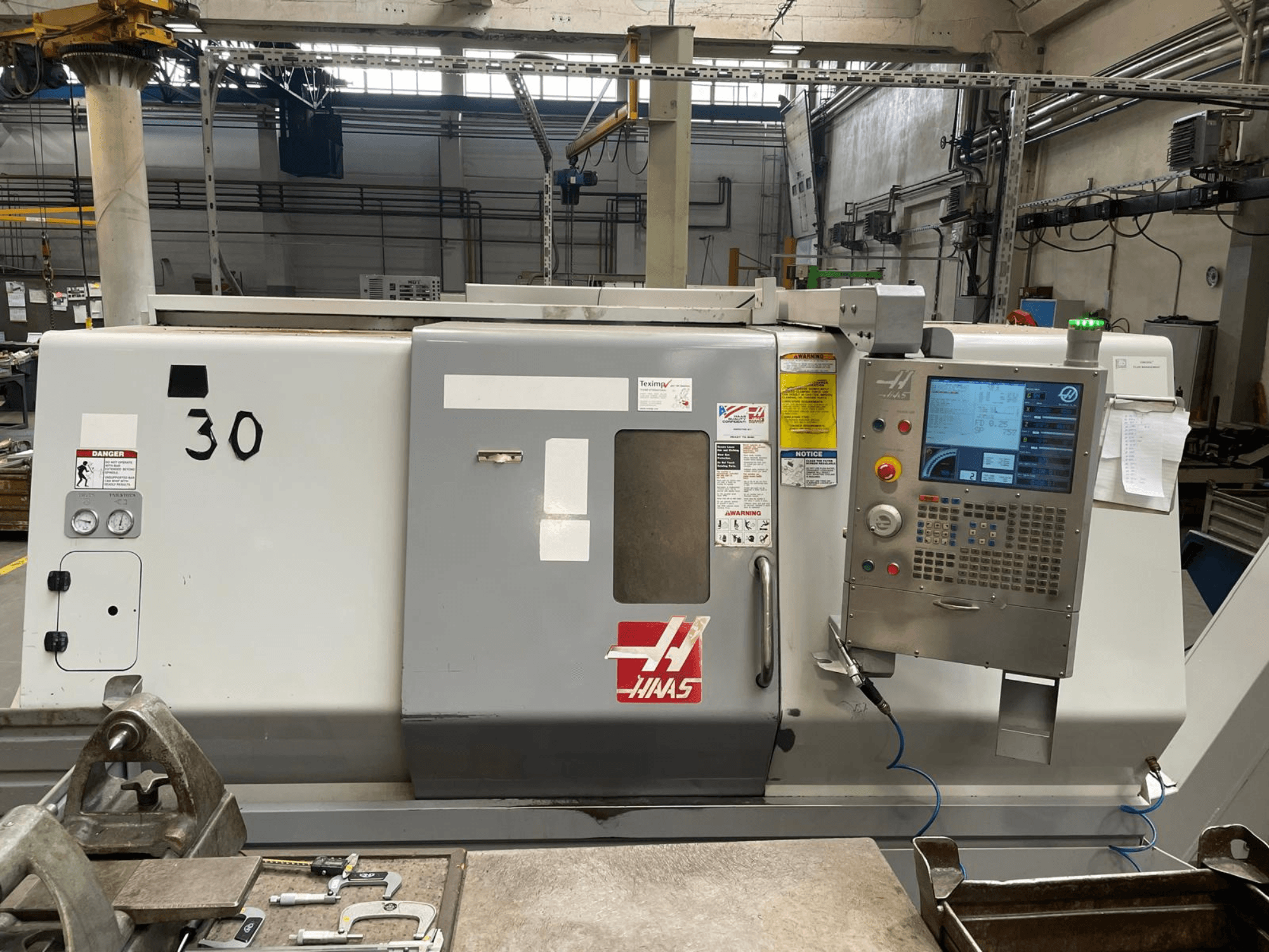 Haas SL-30THE horizontalaus tekinimo staklių vaizdas iš priekio, kuriame matomas skaitmeninis valdymo skydelis, pavojaus ženklai ir modelio numeris 30.