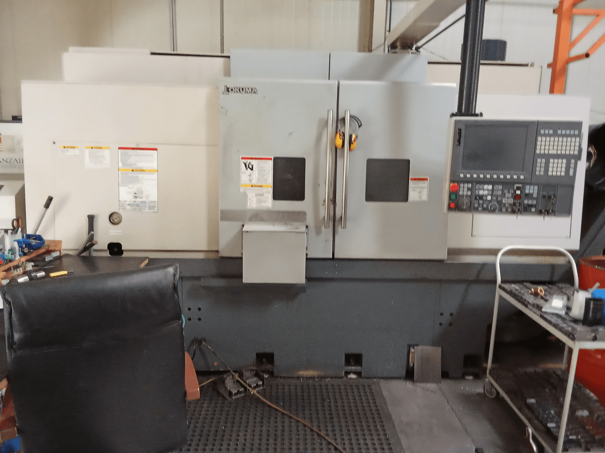 Okuma Genos L300 E-M horizontaliojo tekinimo staklės iš priekio, su valdymo skydeliu ir dvejomis durimis, įrengtos dirbtuvių aplinkoje.